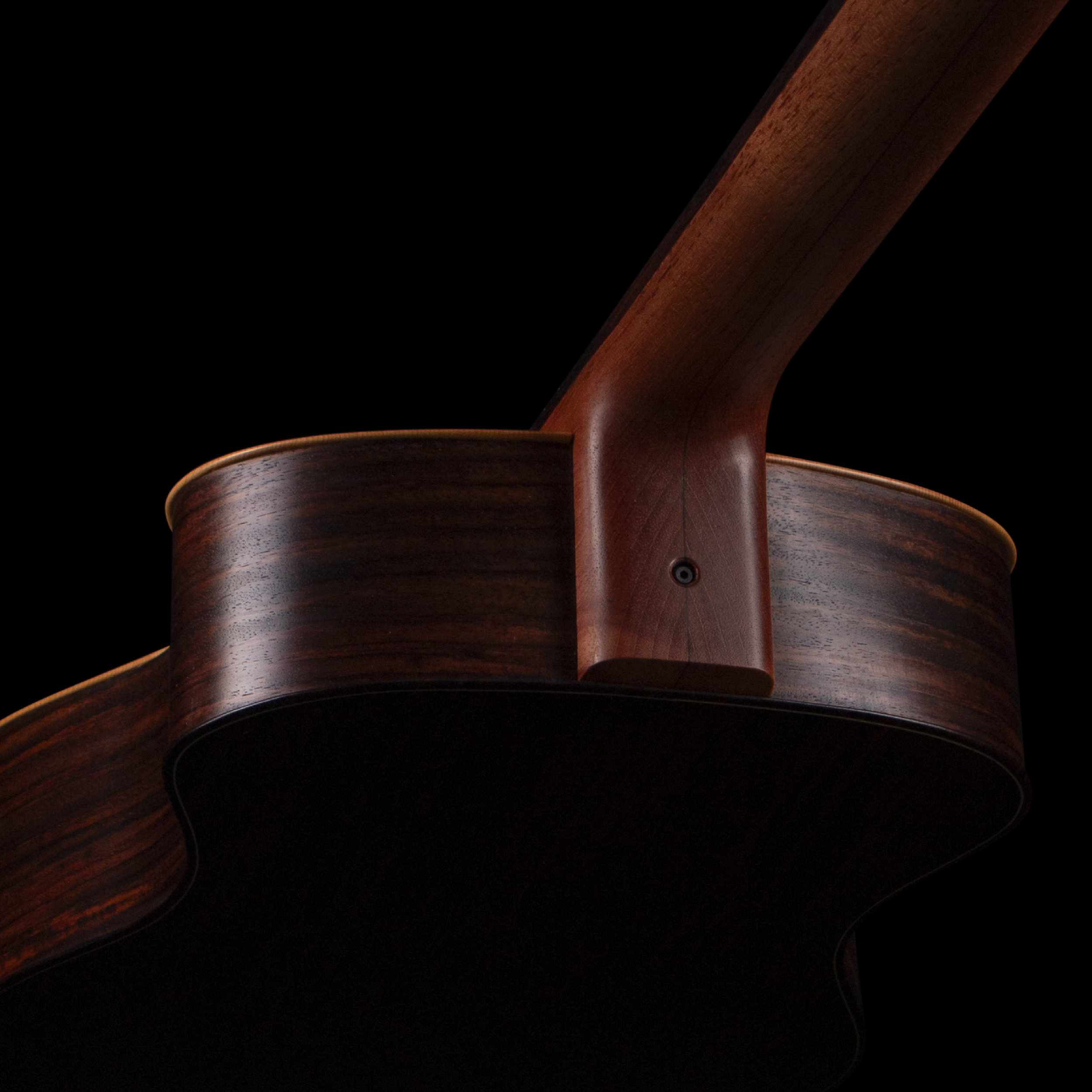 Close-up of a wooden Sankey guitar with a curved backrest against a black background.