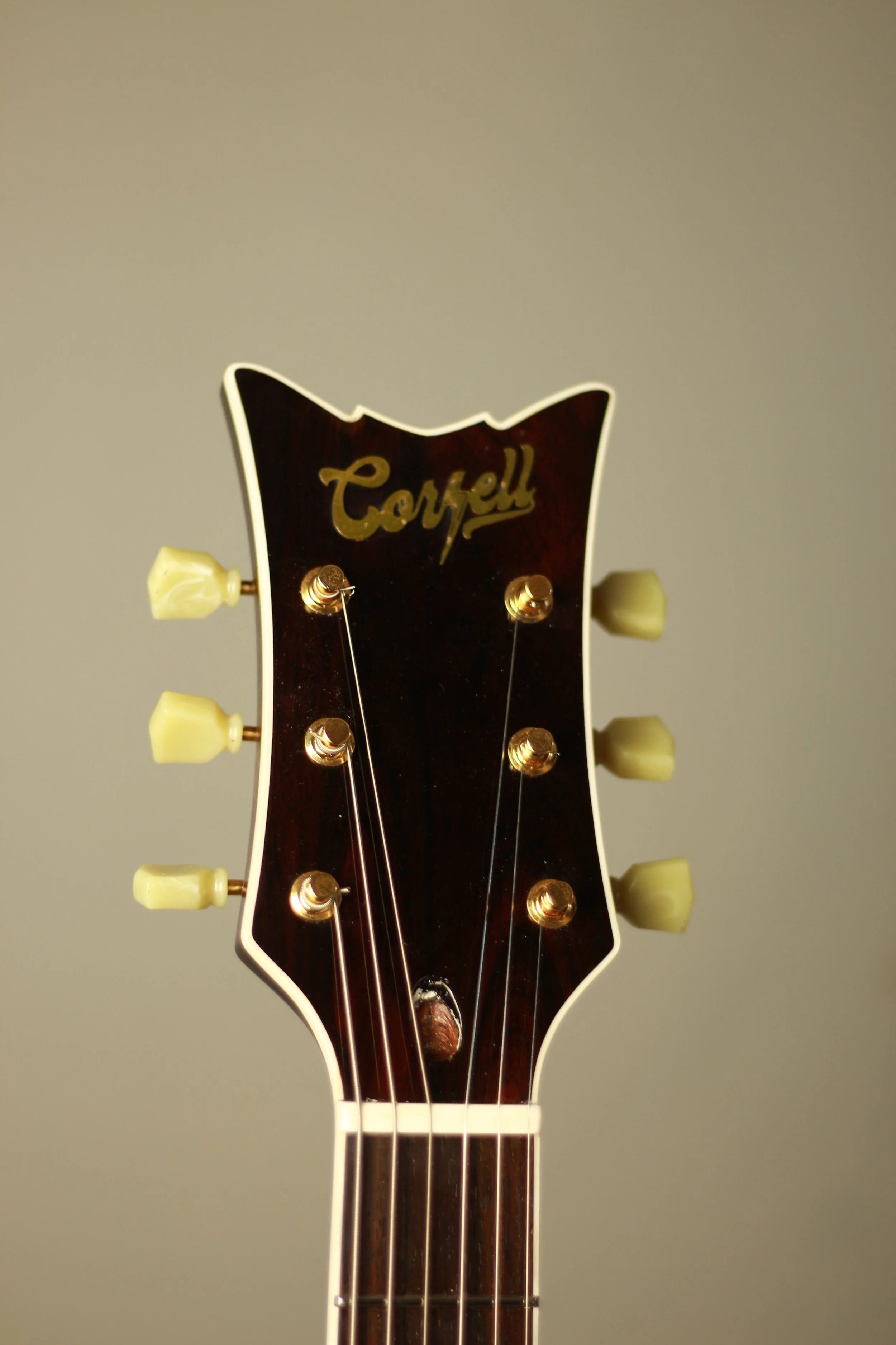 Close-up of a guitar headstock with the brand name 'Corsell' on a dark wood background, six tuning pegs with cream-colored tuning keys, and six metal strings.