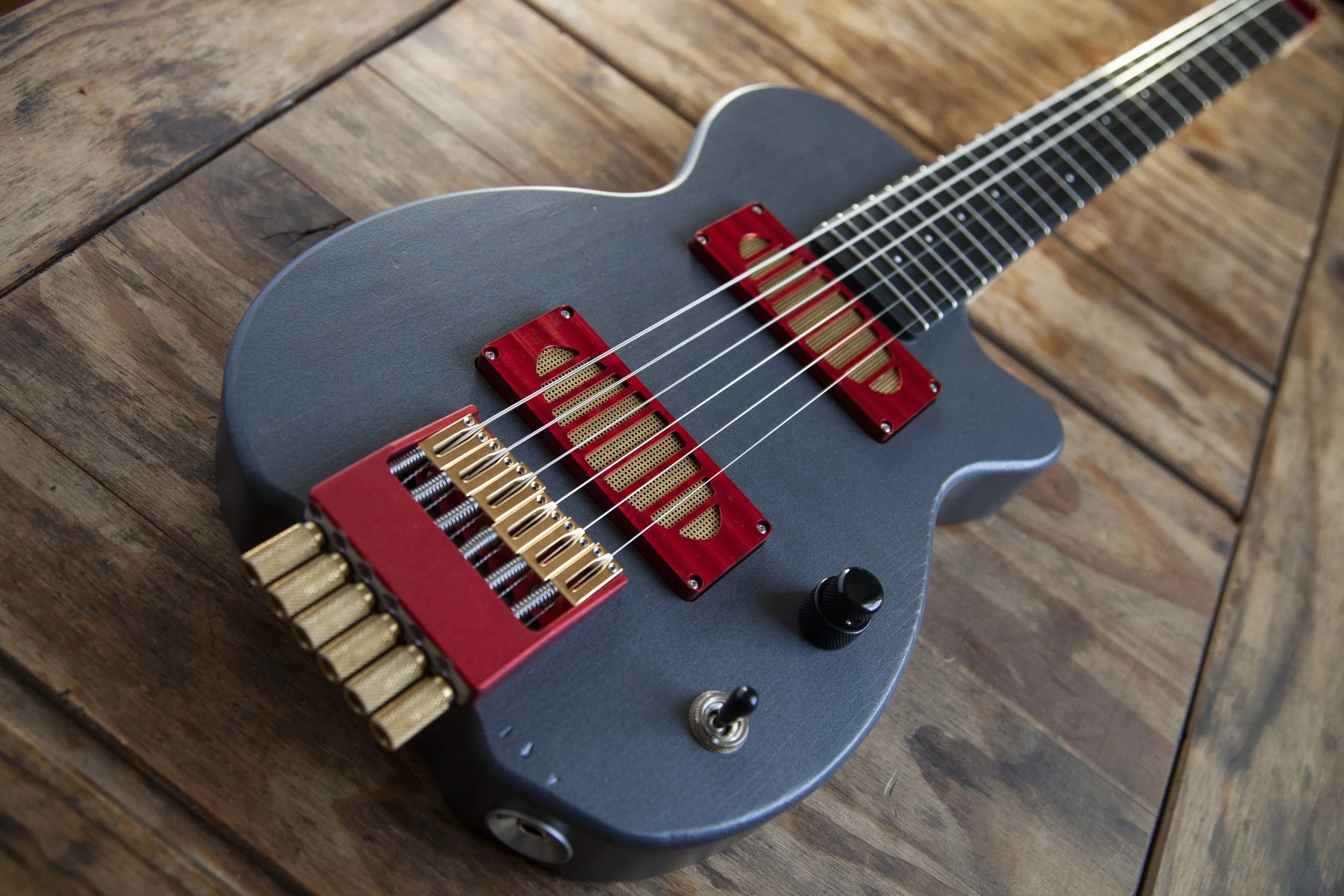 A modern electric Island Instruments guitar with a dark gray body, gold and red pickups, sitting on a wooden surface.
