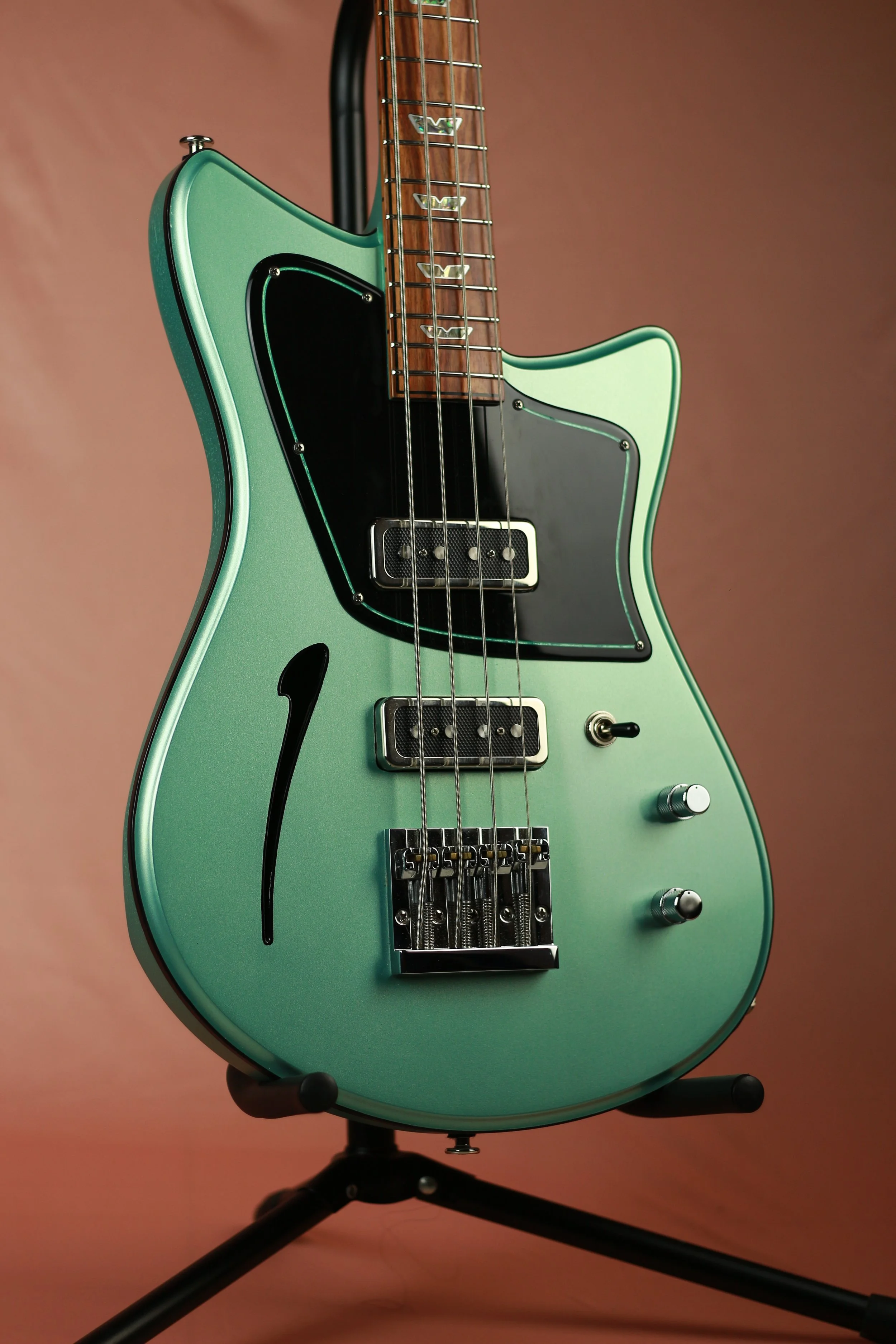 A vintage-style electric Corsell bass guitar with a mint green body, black pickguard, two pickups, and chrome hardware, displayed on a black guitar stand with a peach-colored background.