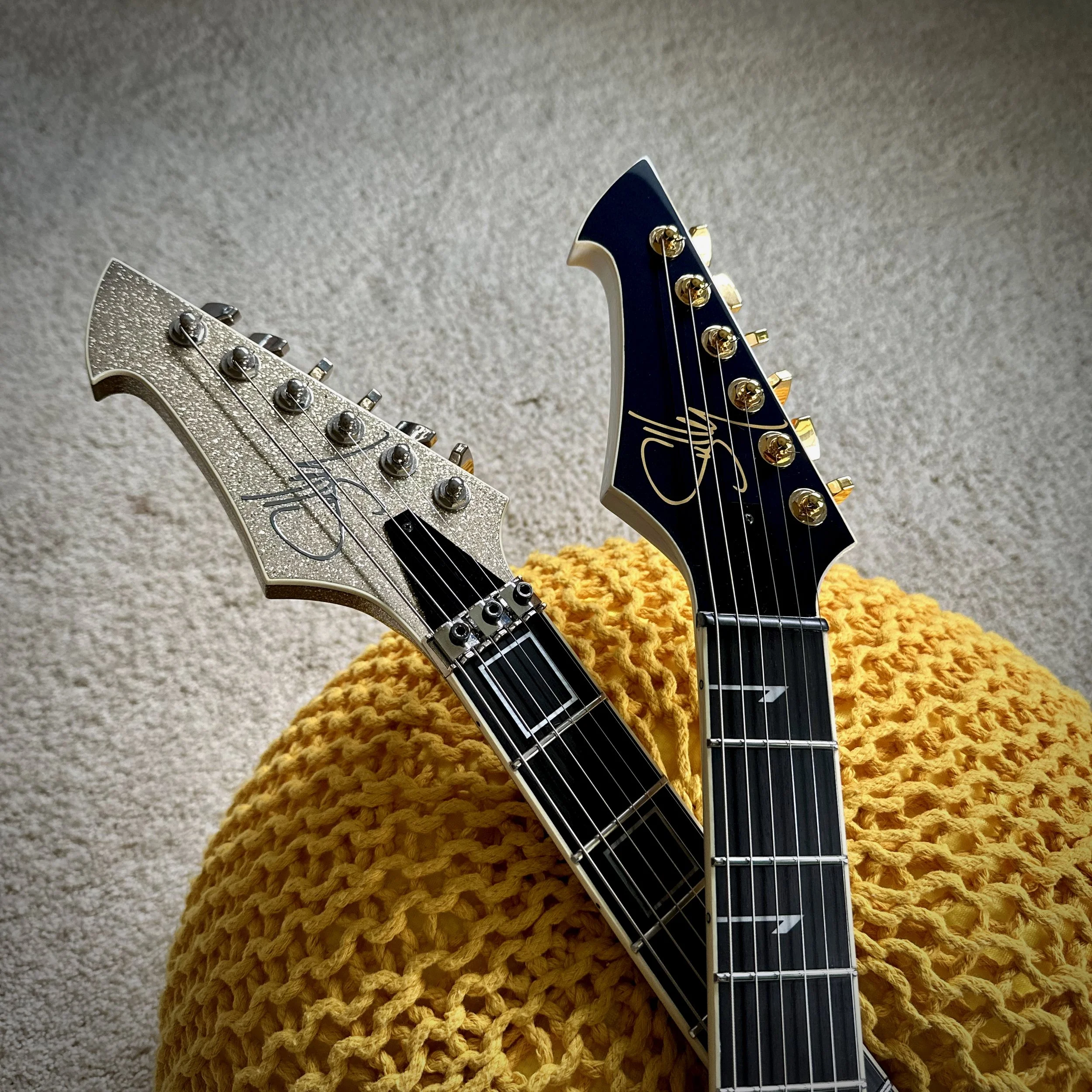 Two electric Sully guitars crossed over a yellow knit blanket on a beige carpet.