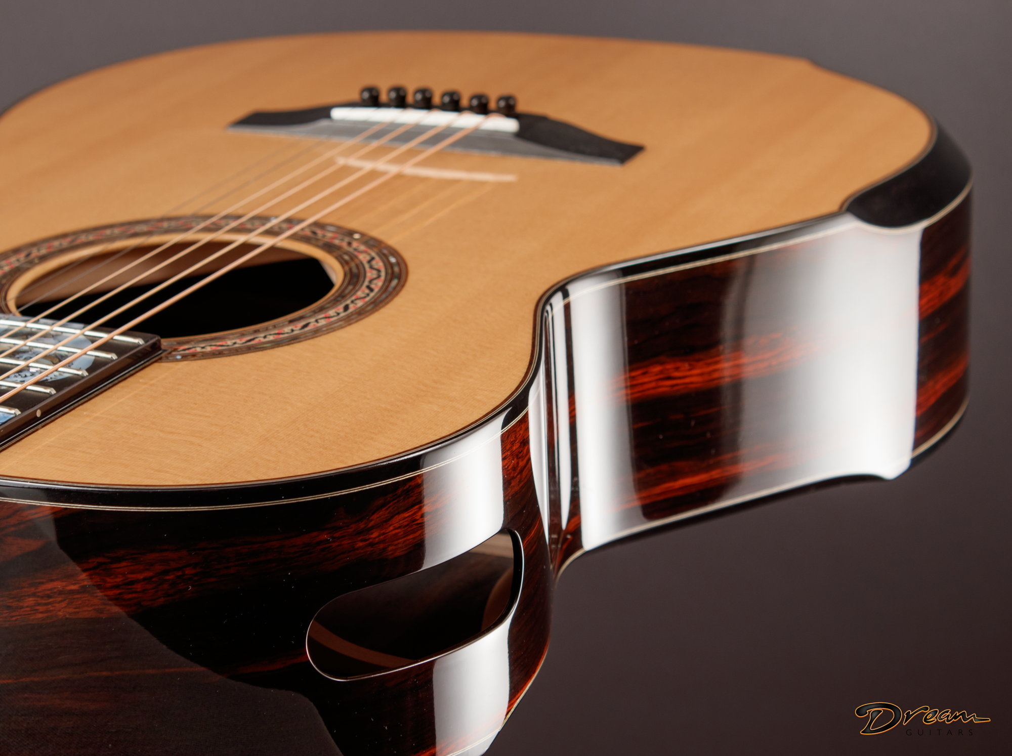 Close-up of a Laskin acoustic guitar with a natural wood finish, black bridge, and decorative rosette around the sound hole, against a dark background.