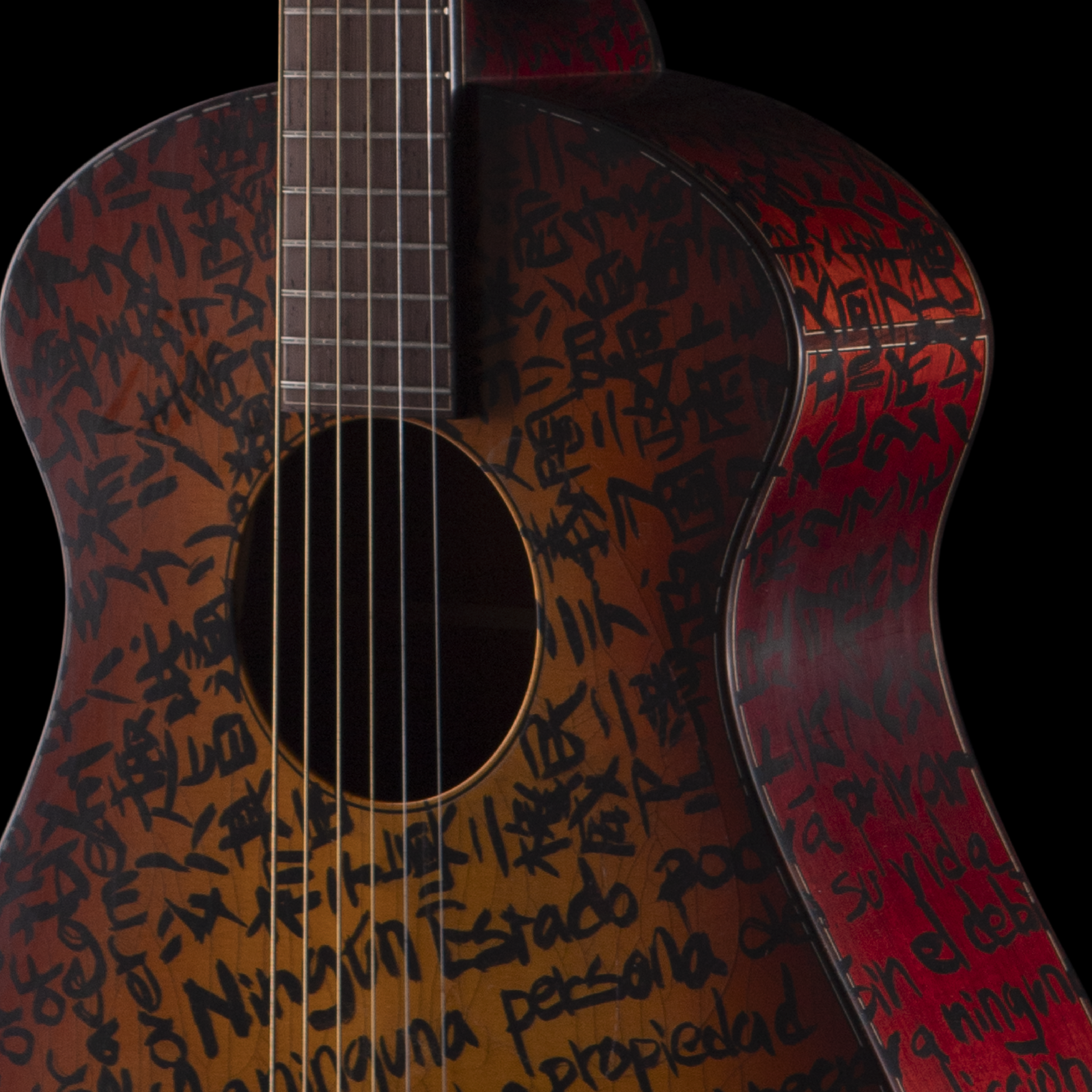 Close-up of a Matsuda guitar with black scribbled writing on its body against a black background.