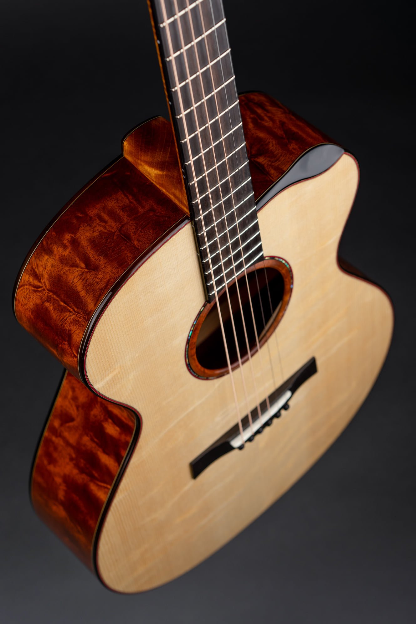 Close-up of an Isaac Jang acoustic guitar with a light-colored top, dark wood neck, and a glossy finish on the sides, set against a black background.