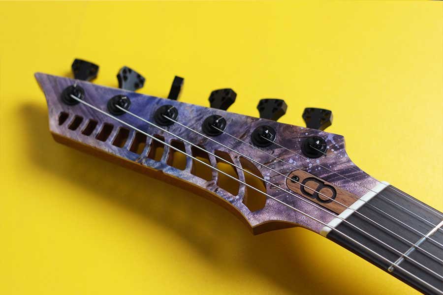 Close-up of an OD Guitar Venus model headstock with black tuning pegs and strings against a yellow background.