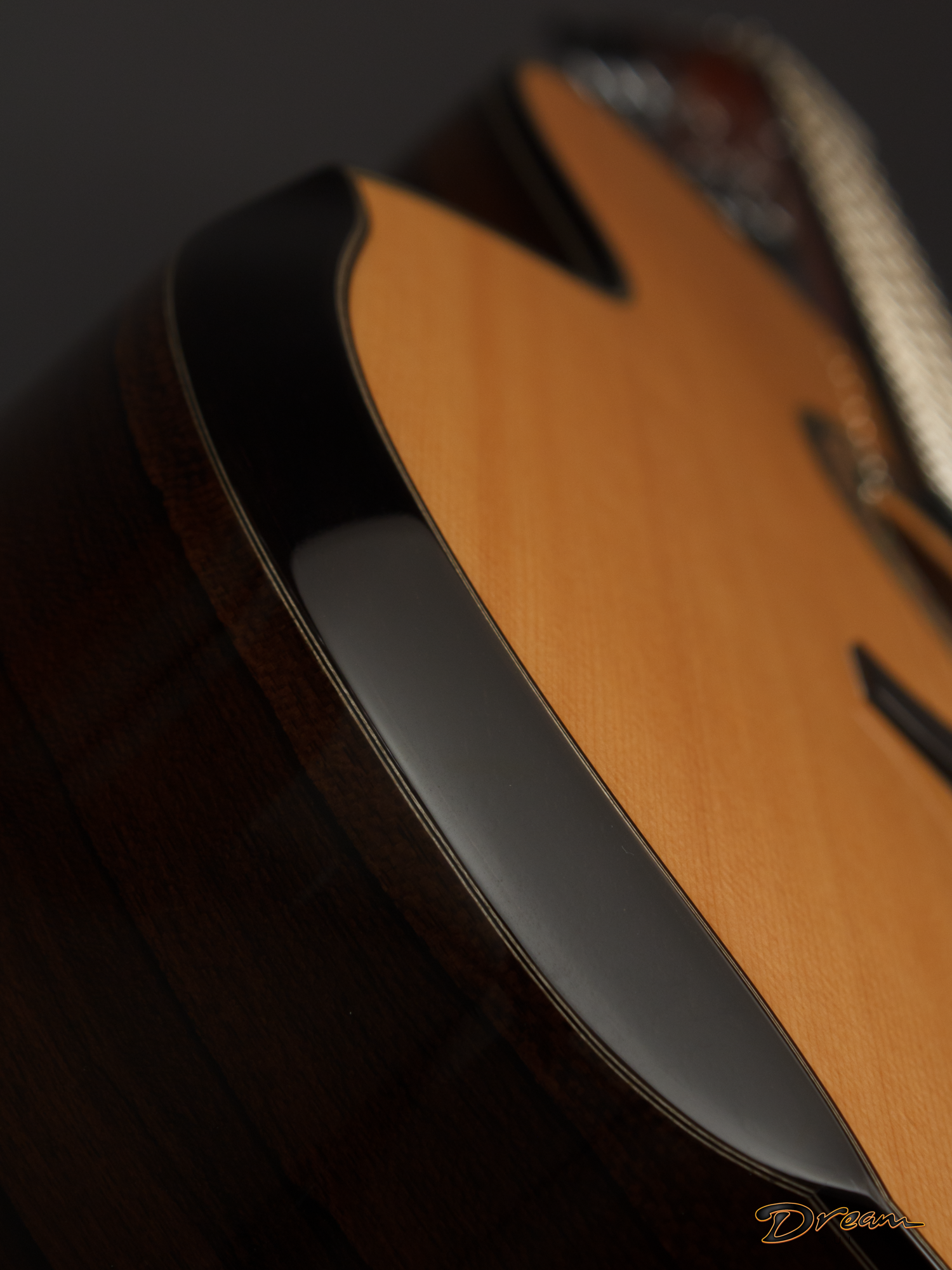 Close-up of a Laskin acoustic guitar's body with a black pickguard, set against a dark background, featuring the word "Dream" written in cursive at the bottom right corner.