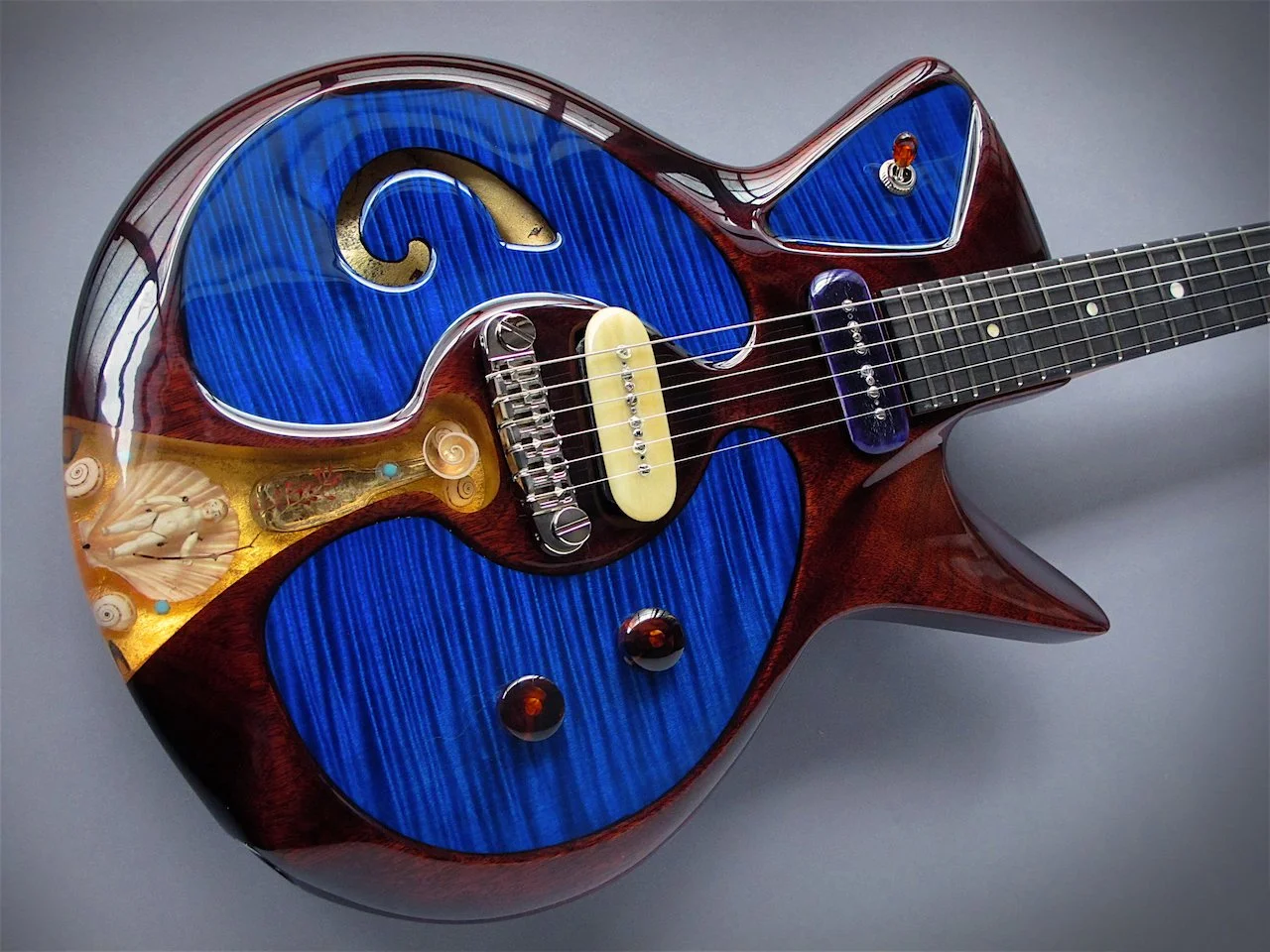 A colorful electric Spalt guitar with a mixed design of blue, brown, and gold patterns and embellishments, featuring a unique shape and intricate details.