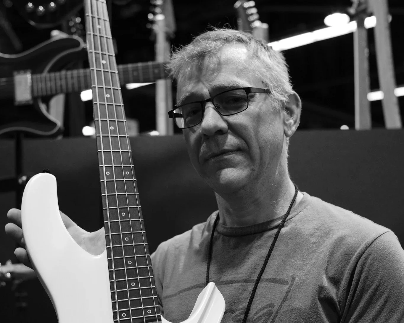 Jerome Little, a man with glasses and gray hair holding a white electric guitar, in a setting with other guitars in the background.