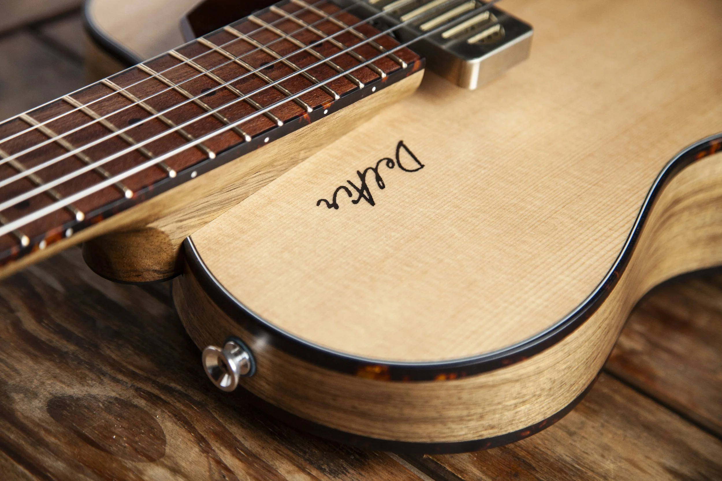 Close-up of a wooden acoustic Island Instruments guitar with the brand name 'DelAir' on the body, showing part of the fretboard and strings, resting on a wooden surface.
