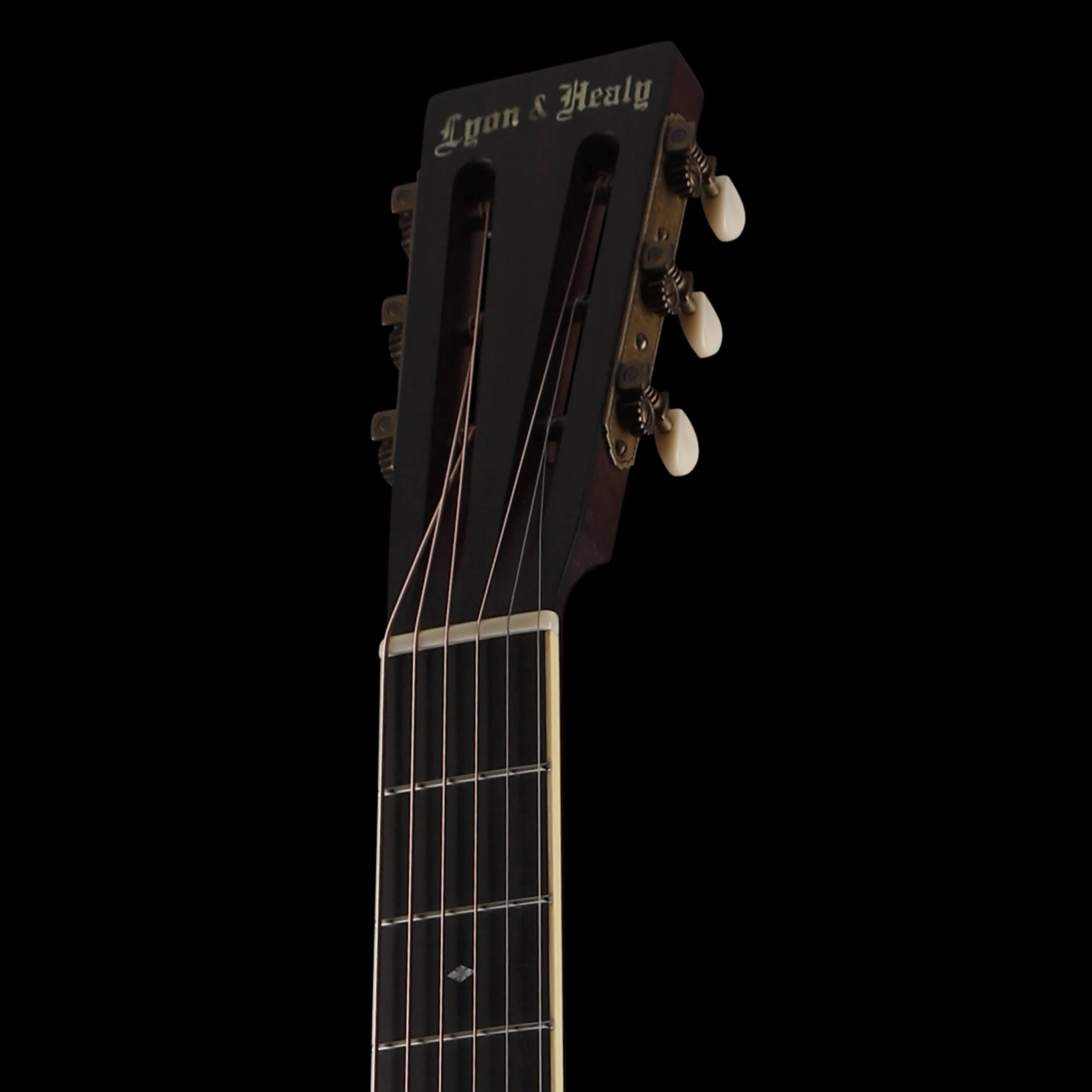 Close-up of the headstock of a vintage acoustic guitar with tuning pegs, strings, and a black label reading 'Lyon & Healy' on a dark background.