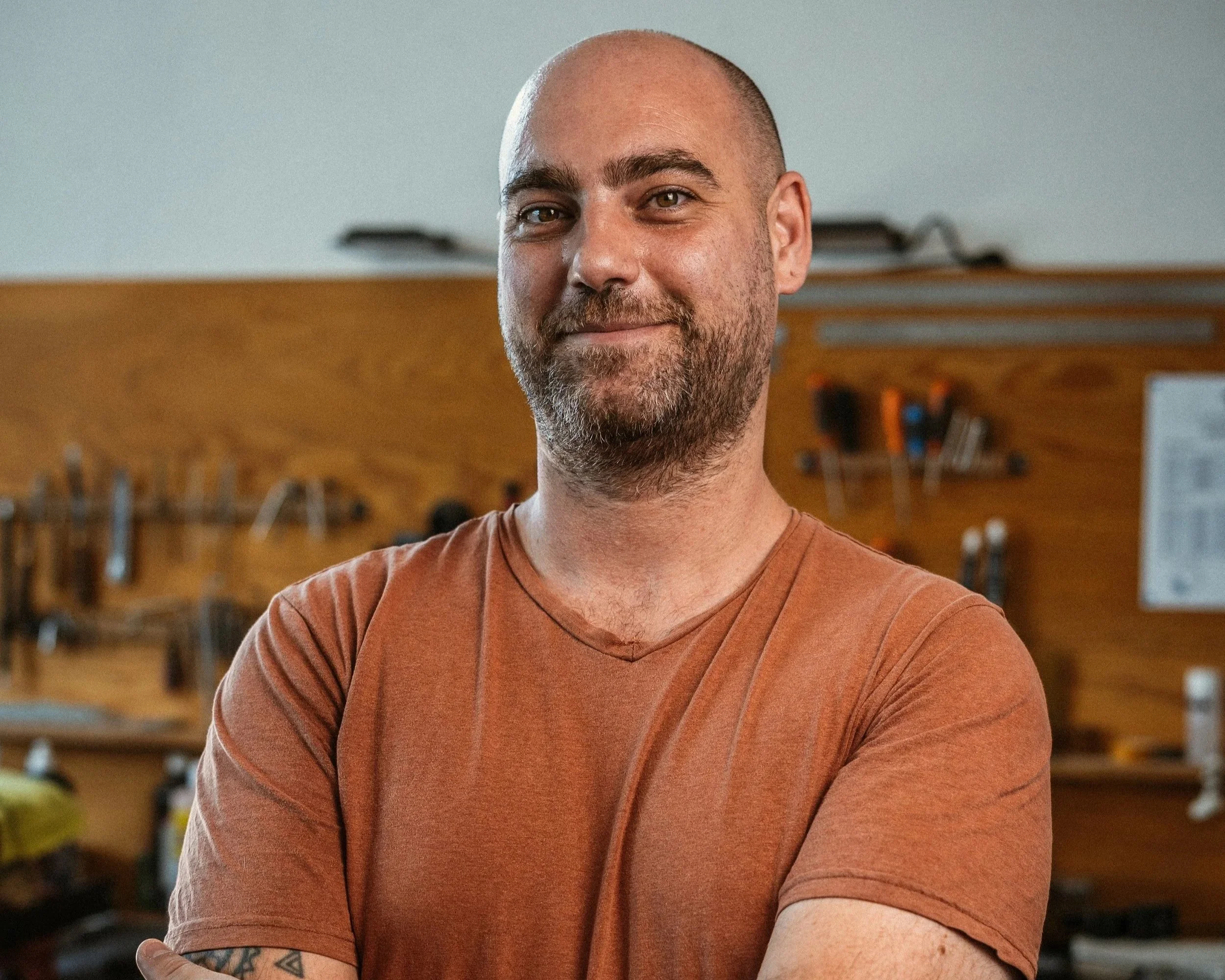 Filippo Pavan a man with a beard and a shaved head smiling with arms crossed in a workshop background.