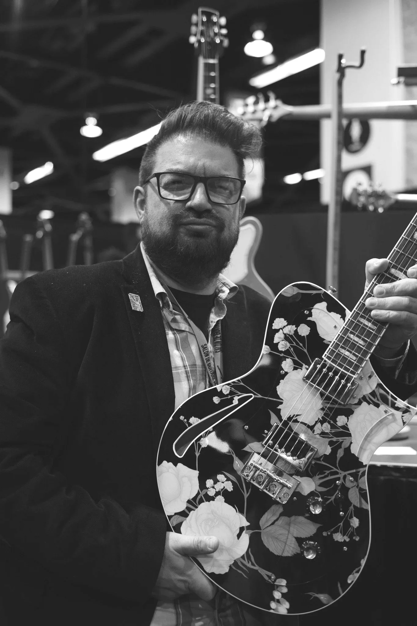 Doug Kauer with glasses and a beard holds a floral design electric guitar.