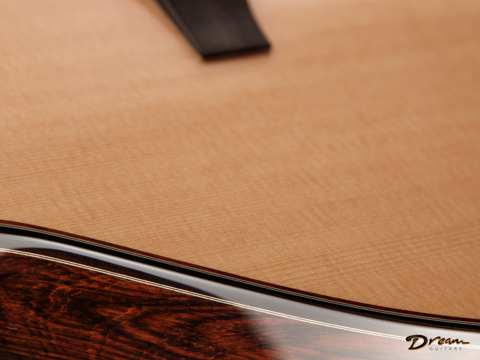 Close-up photo of a wooden Laskin guitar body showing the transition between a light natural wood finish and darker polished wood, with a partial logo reading 'Dream Guitars' in the bottom right corner.