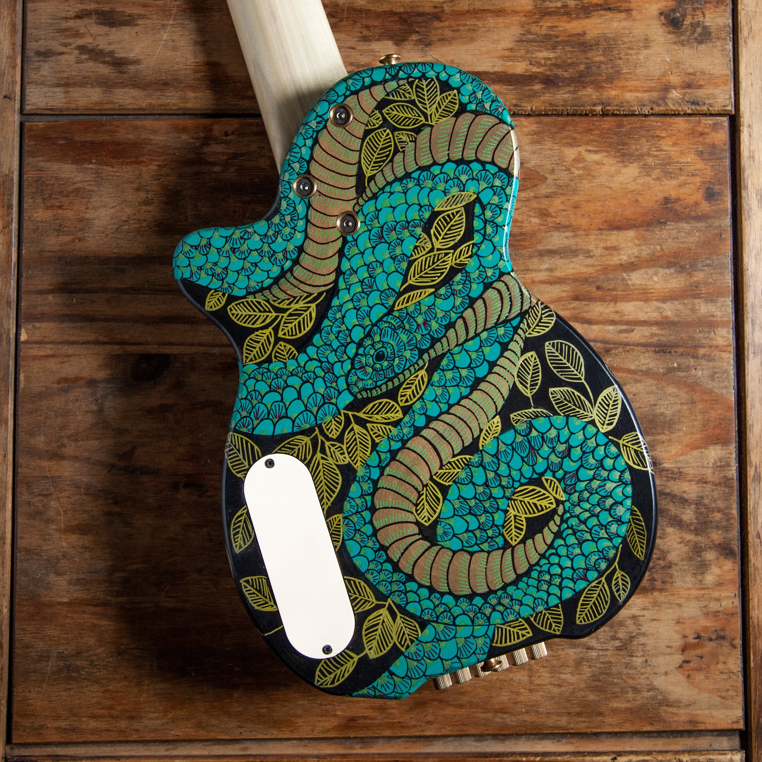 An Island Instrument guitar with a colorful, intricate leaf and floral pattern on its body, resting on a wooden surface.