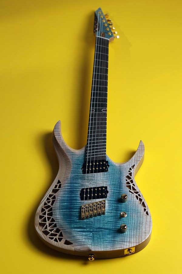 OD Guitars electric with a blue and natural wood finish, black pickups, gold hardware, and decorative cutouts on the body, set against a yellow background.