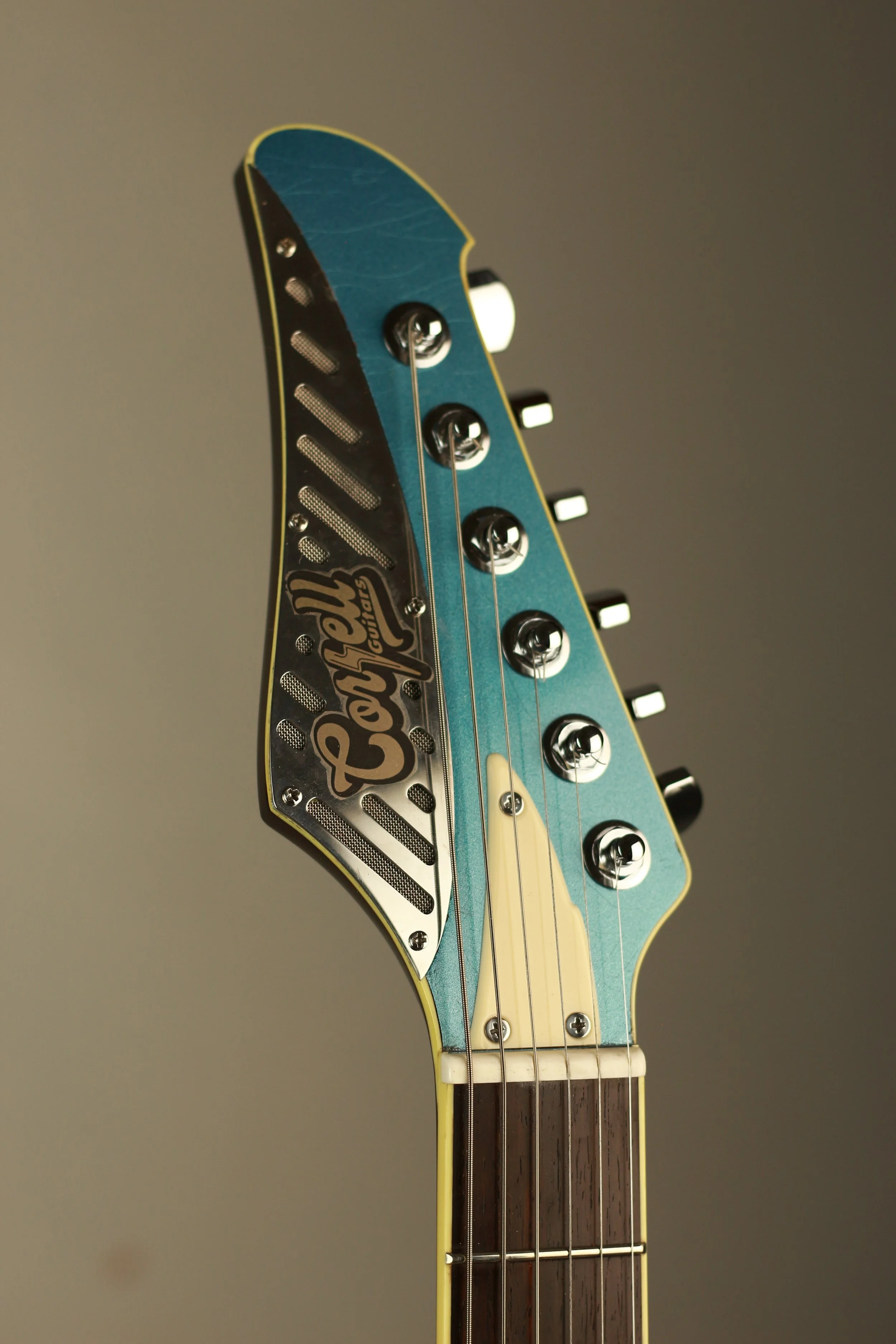 Close-up of the headstock of a guitar with the brand name 'Corsell' on a metallic plate, blue color, six tuning pegs, and strings.