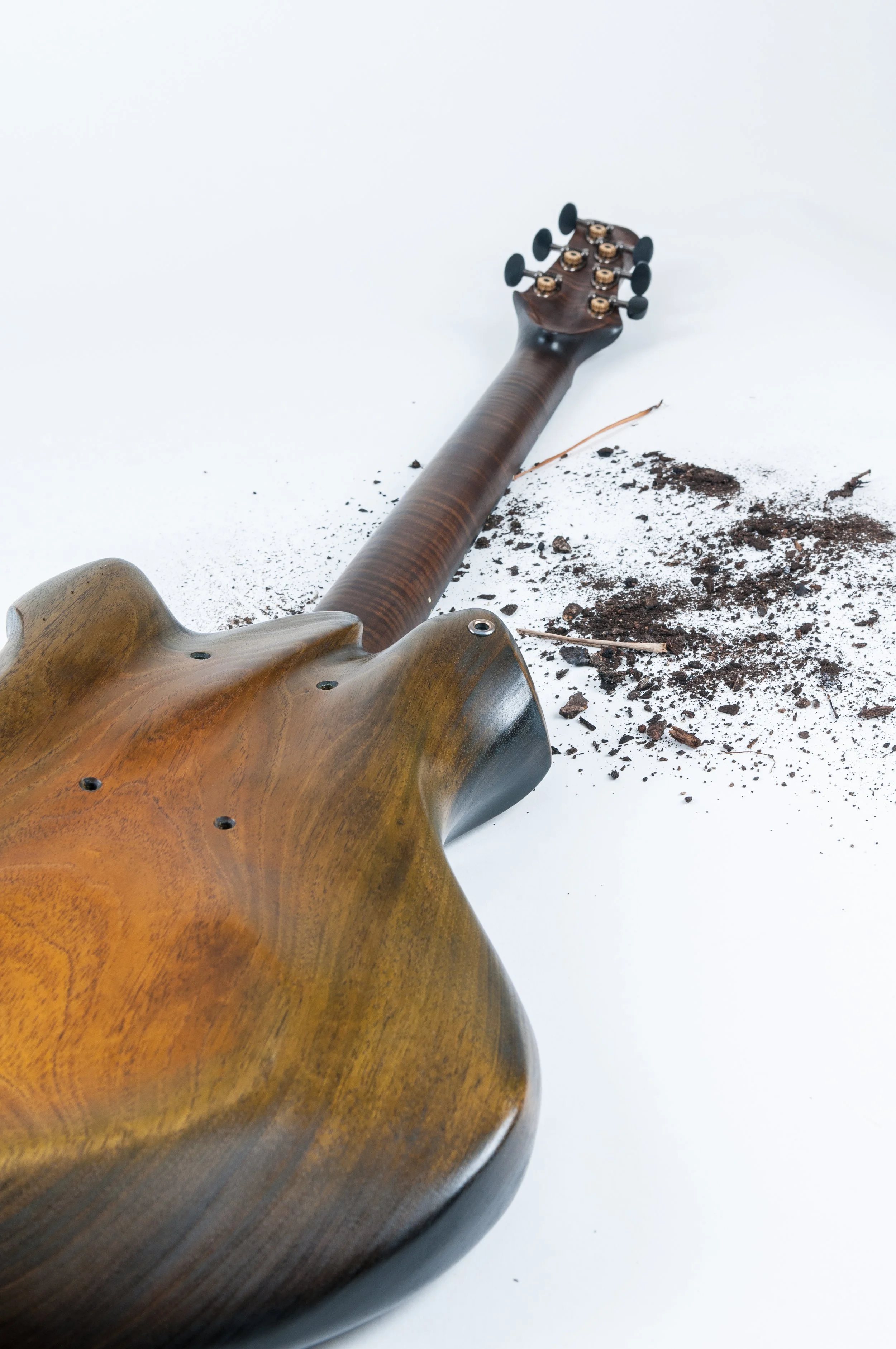 An electric Ergon guitar lying on the white floor, damaged with soil and dirt around the body and neck.