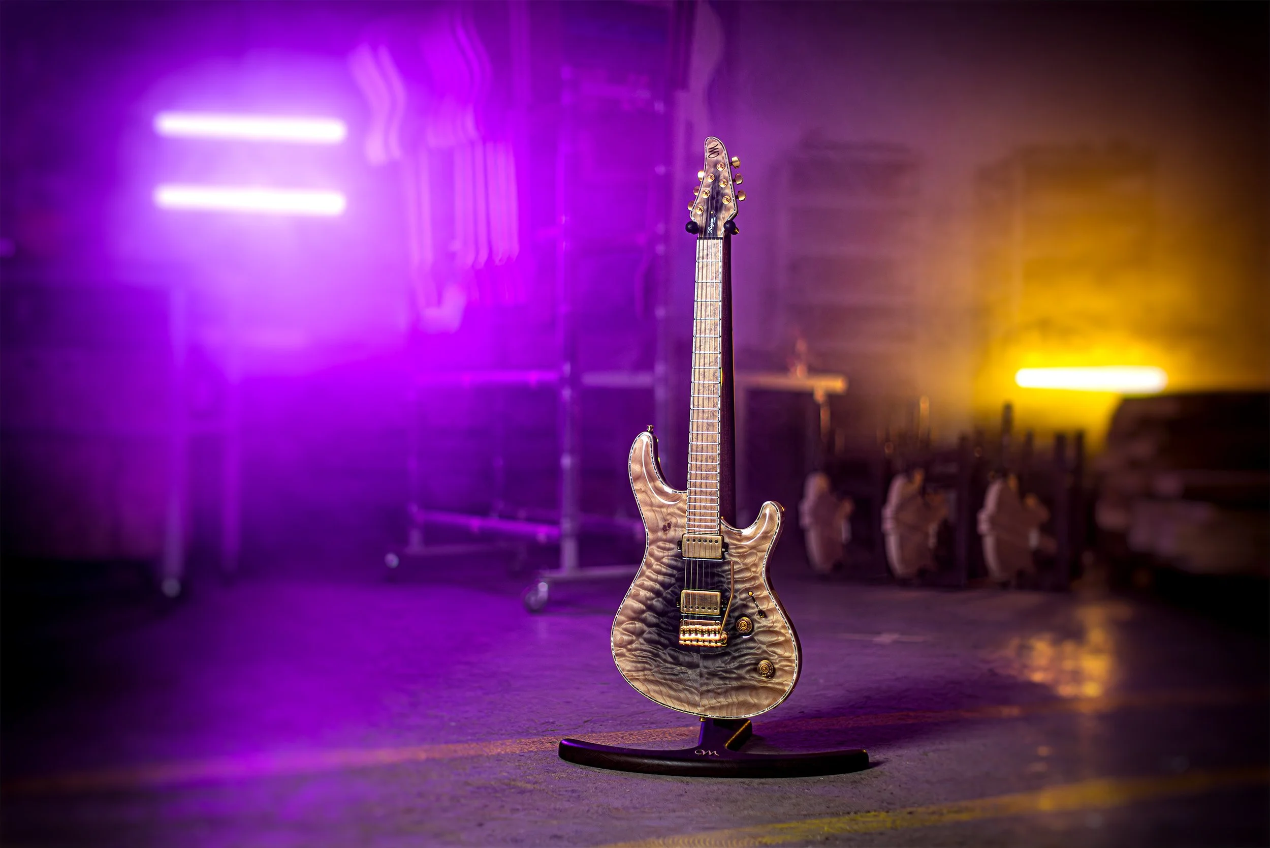 An electric Mayones guitar with a quilted maple top on a guitar stand in a dimly lit room with purple and yellow neon lights.