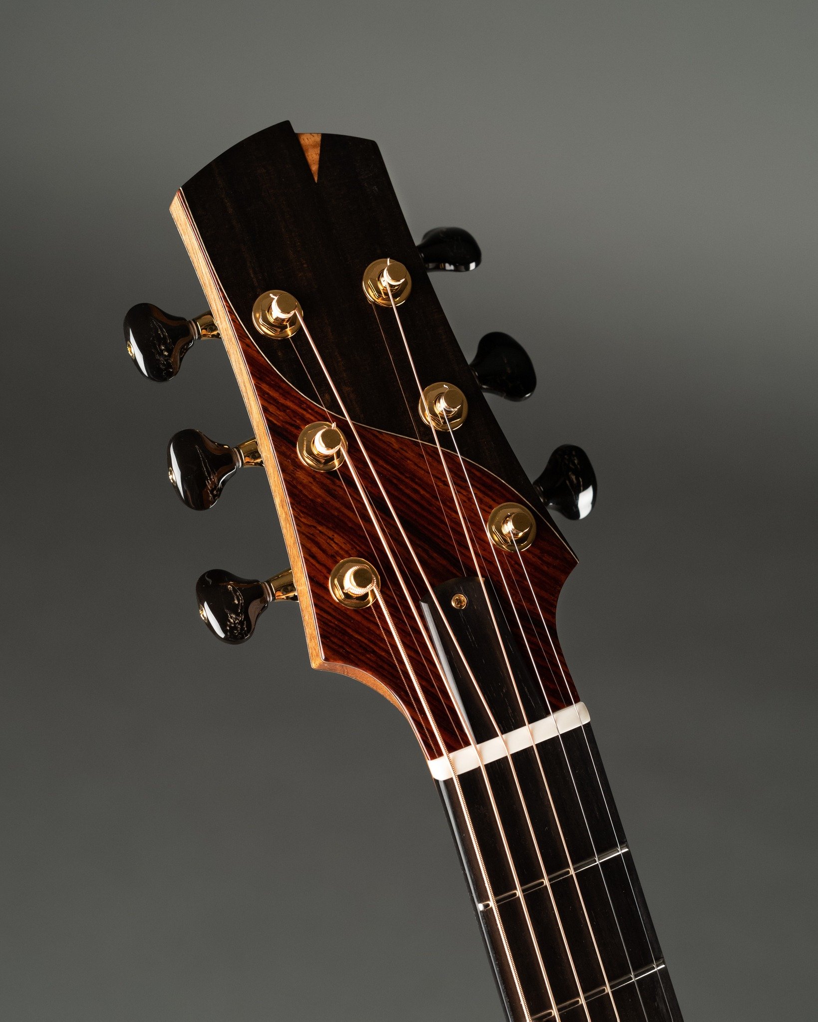Close-up of an Isaac Jang guitar headstock with six tuning pegs, set against a plain gray background.