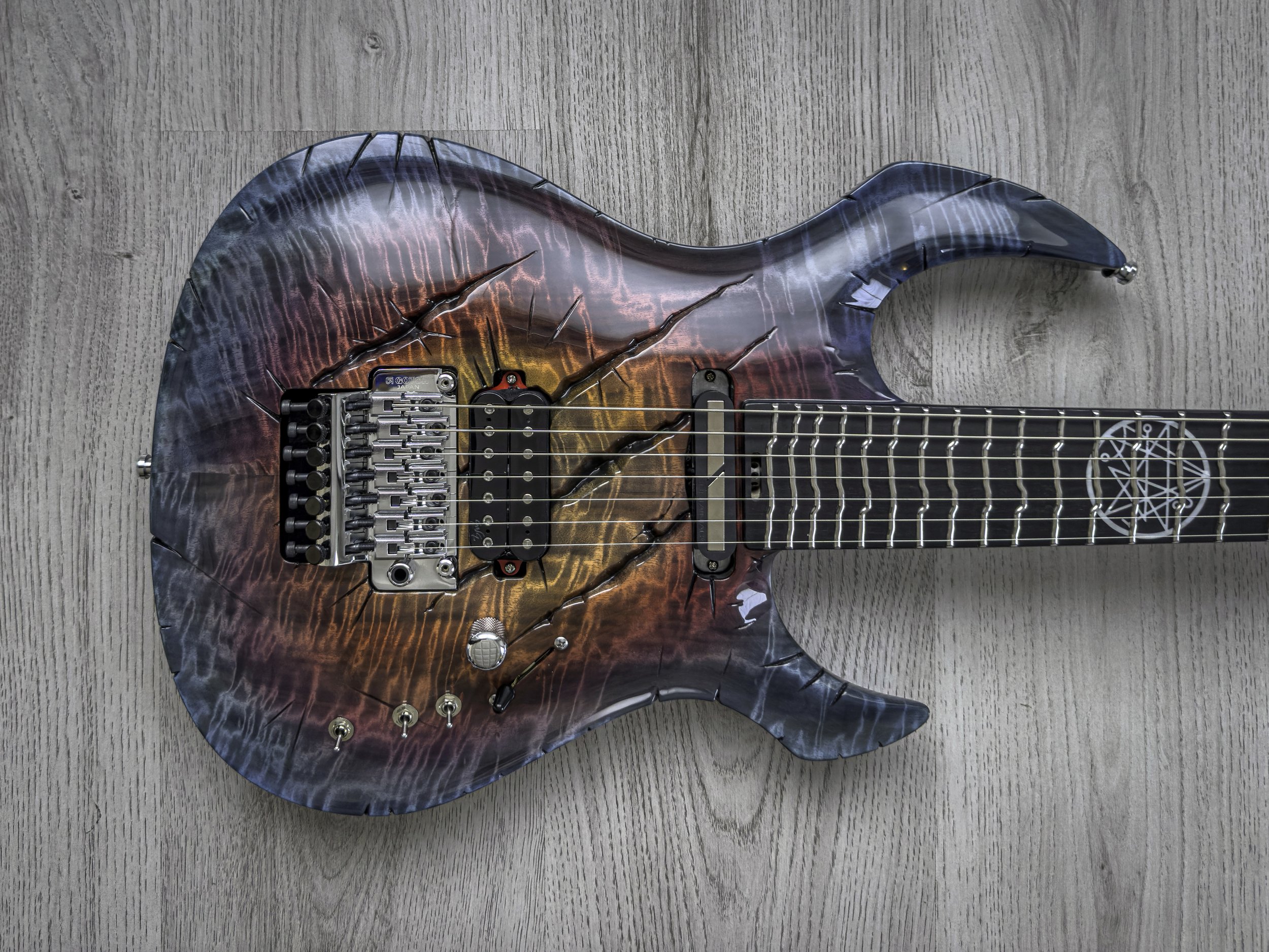 GNG Giulio Negrini electric guitar with a graphic design resembling a dragon's wing, featuring flames and cracks, on a wooden surface.