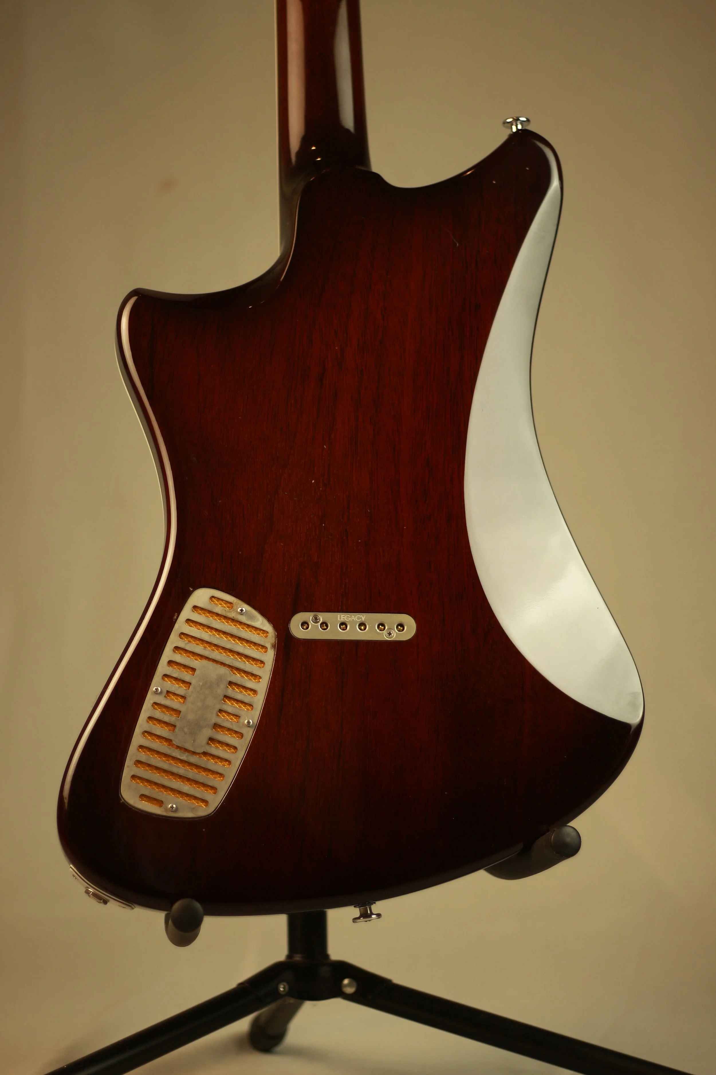 Back of a vintage electric Corsell guitar with a dark wood finish, mounted on a black stand.