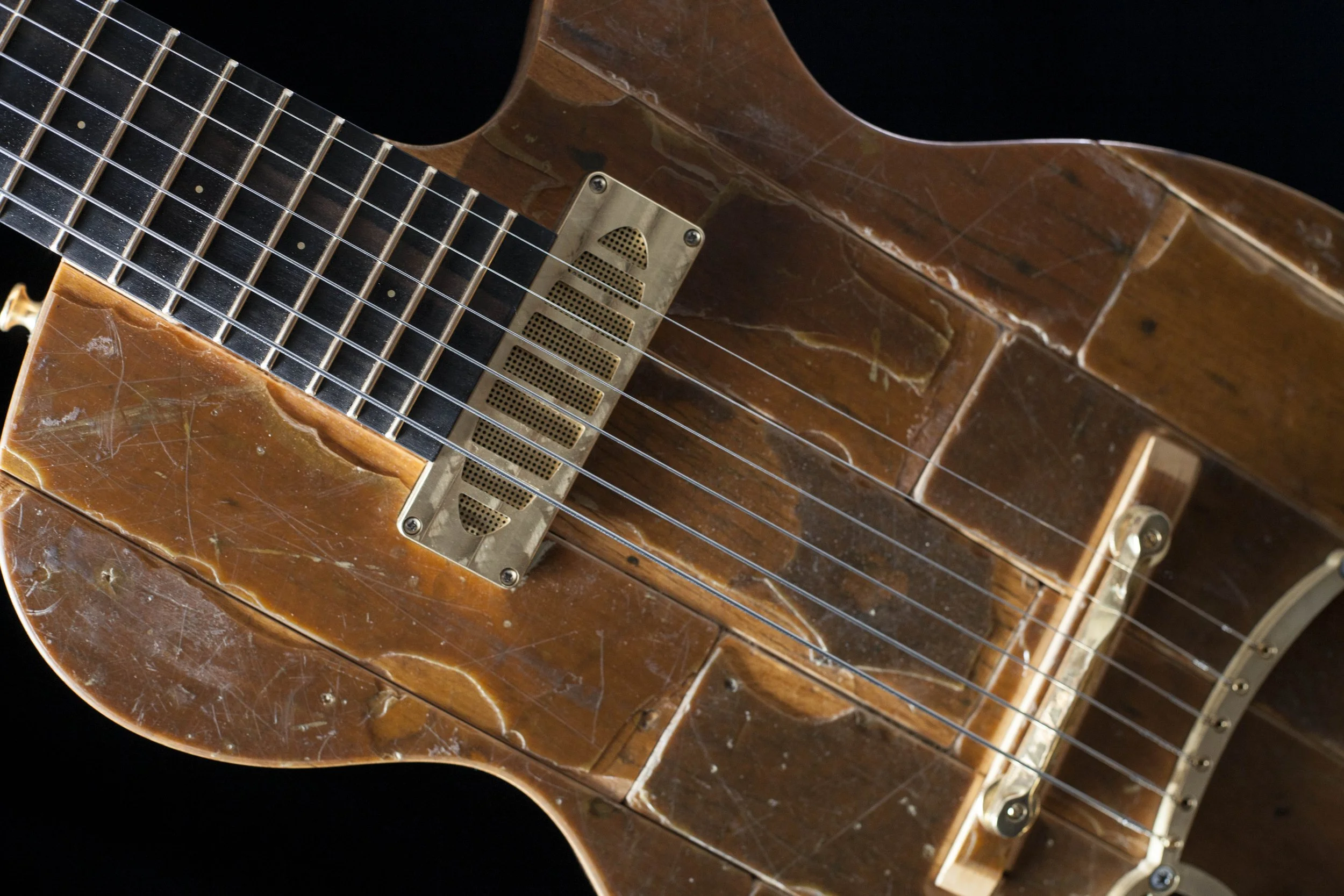 Close-up of a vintage electric Island Instruments guitar with a distressed brown finish, metal pickguard, and six strings against a black background.