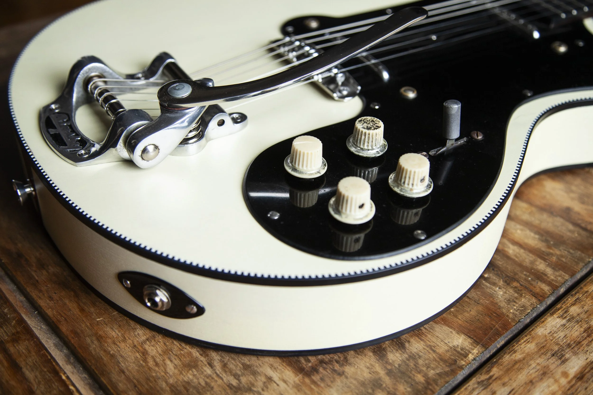 Close-up of a vintage electric Island Instruments guitar's bridge, control knobs, and part of the body on a wooden surface.