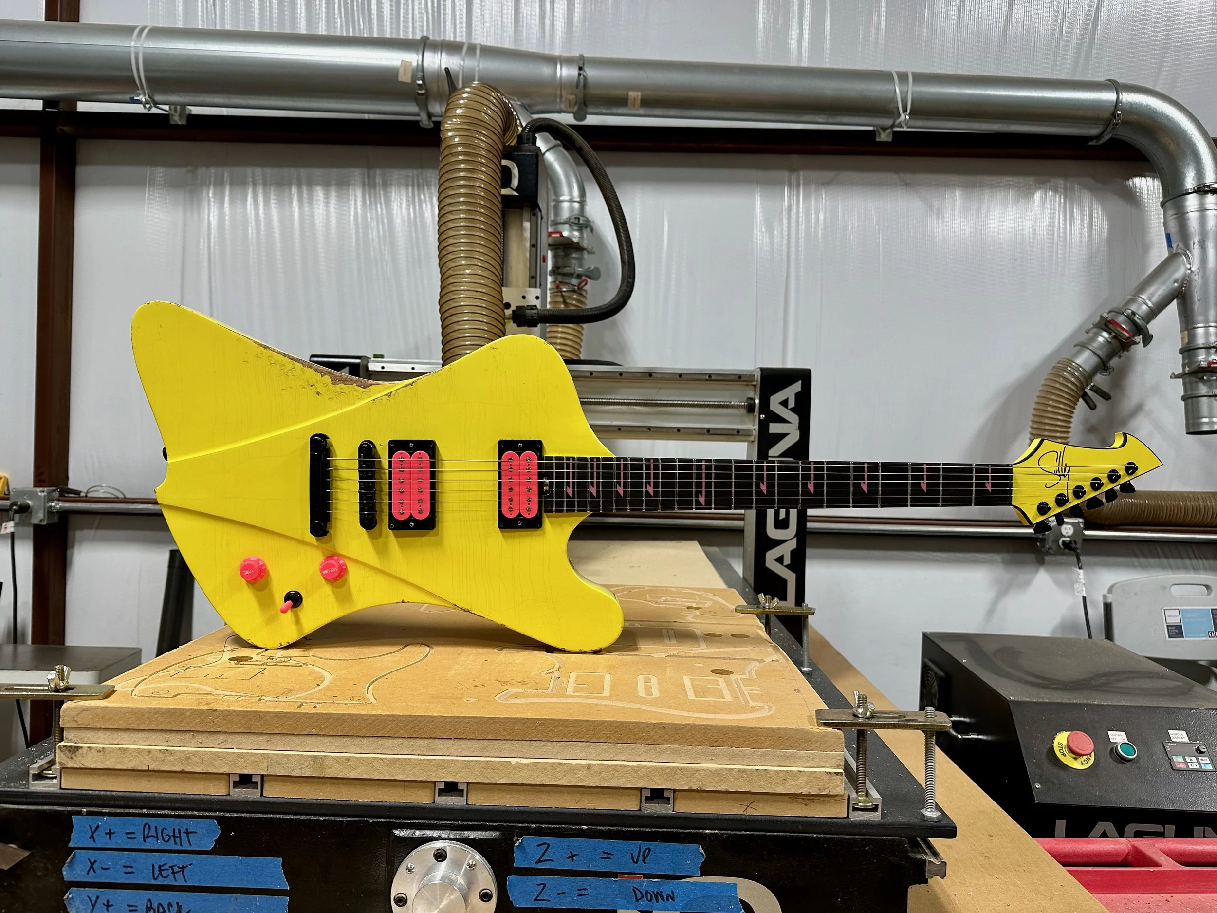 Yellow electric Sully guitar on a workbench with mechanical and industrial equipment in the background.