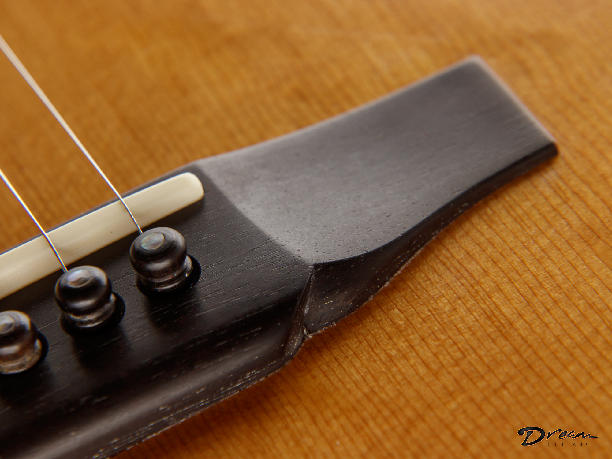 Close-up of a classical wooden Laskin guitar's bridge, strings, and saddle on a wooden surface. The image showcases detail of the guitar's construction.