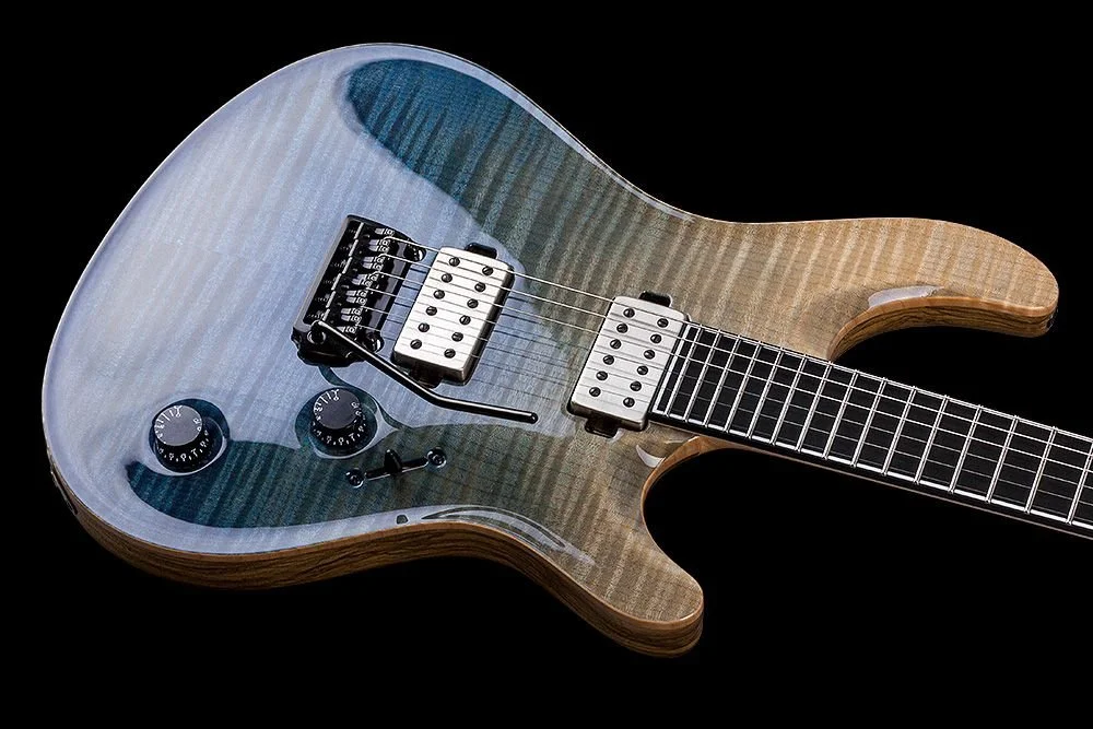 Electric Mayones guitar with a transparent body, striped wood pattern, black and white pickups, and black knobs on a black background.