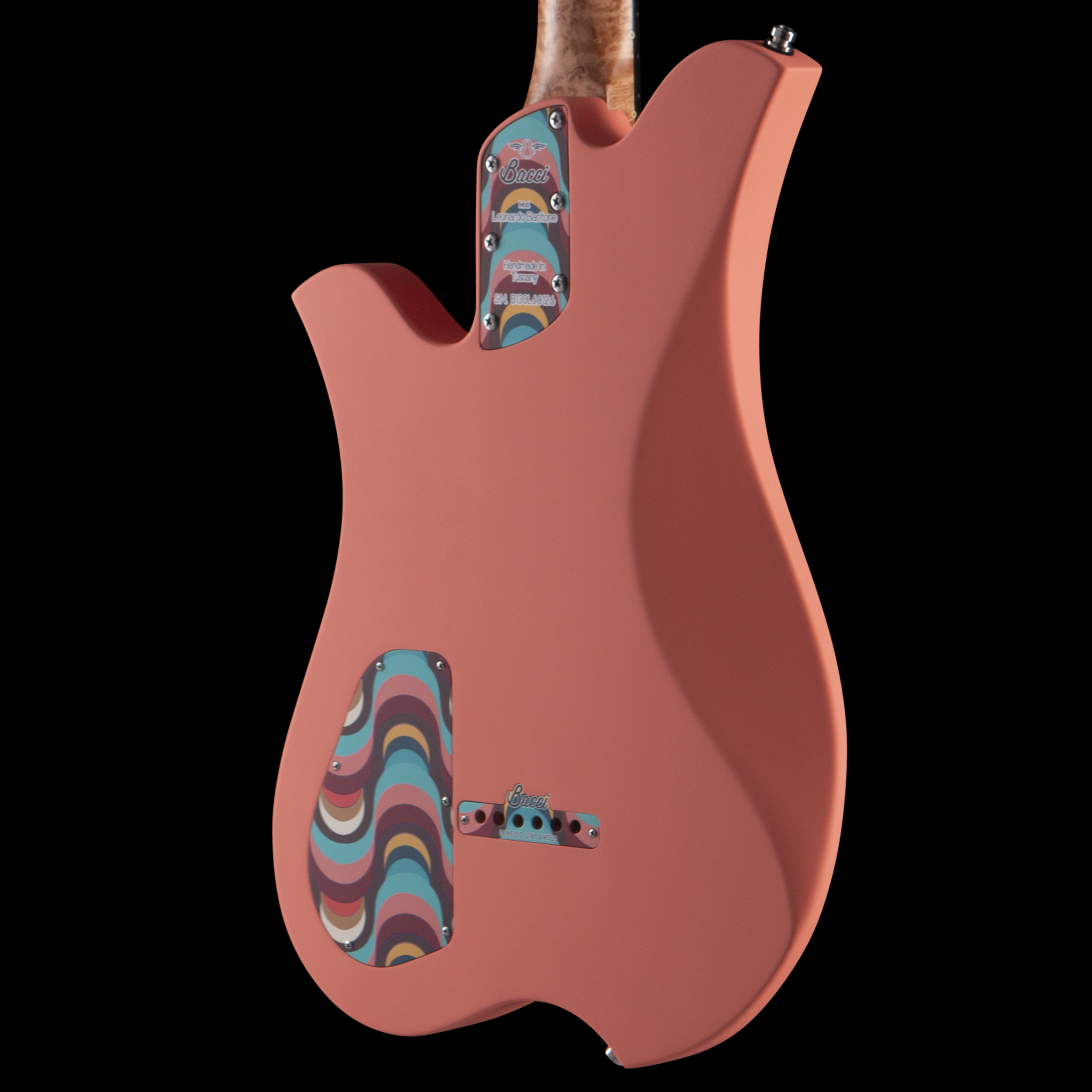 Close-up of a pink electric Bacci guitar with a colorful, patterned pickguard and a small label indicating it is handmade in Tuscany by Bacci.