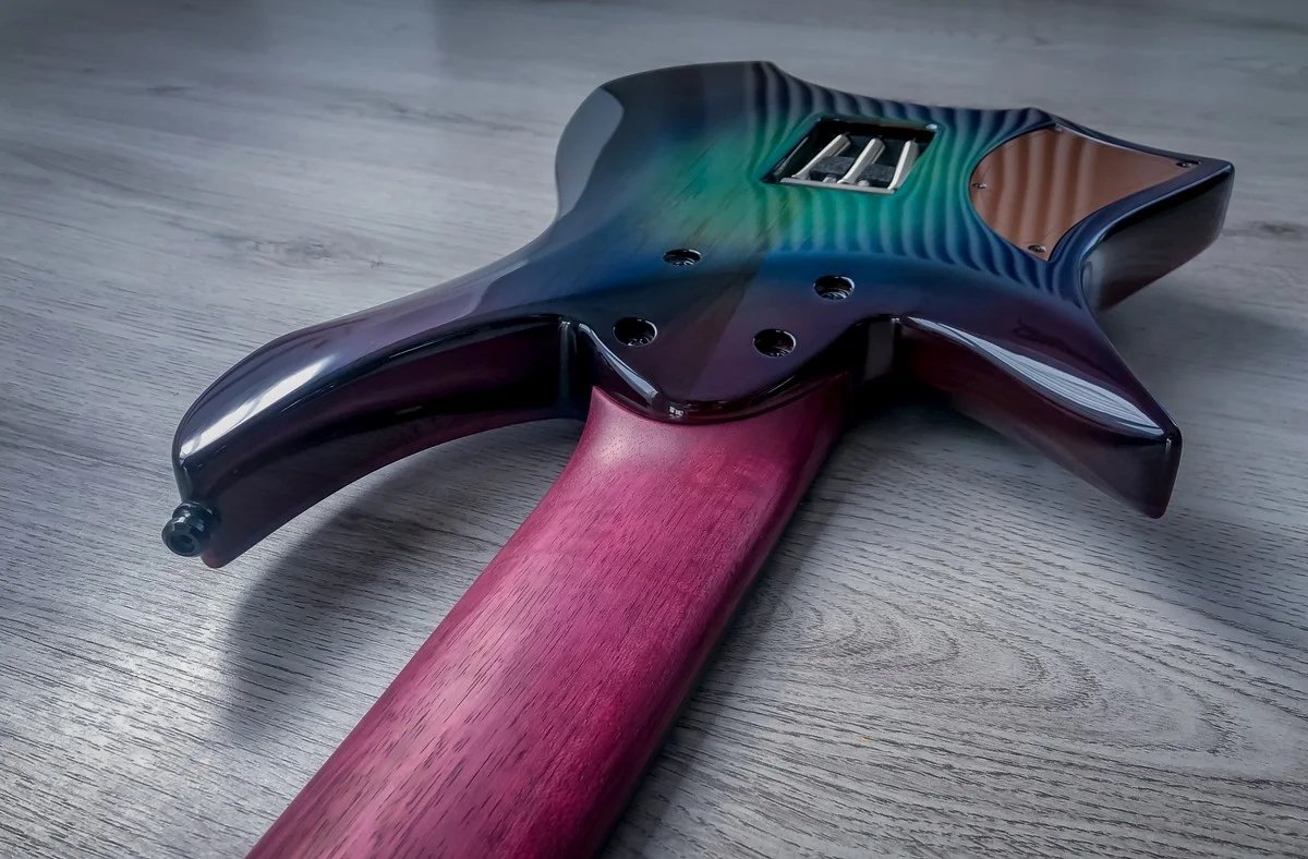 Back view of a GNG Giulio Negrini guitar on a wooden floor, showcasing a gradient finish transitioning from blue to green with a purple neck.