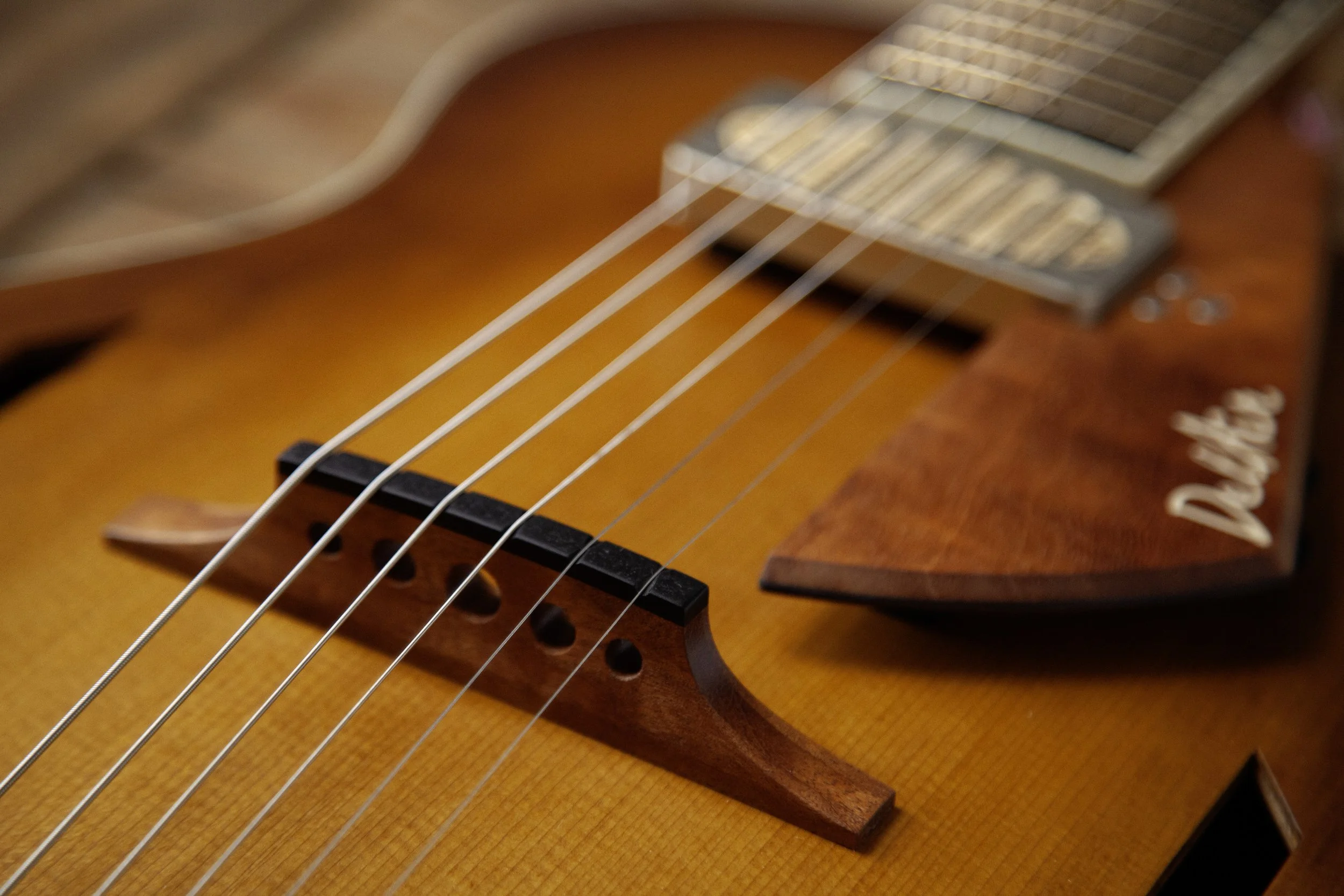 Close-up of an acoustic Island Instruments guitar's bridge with six strings and a pick resting on the body.