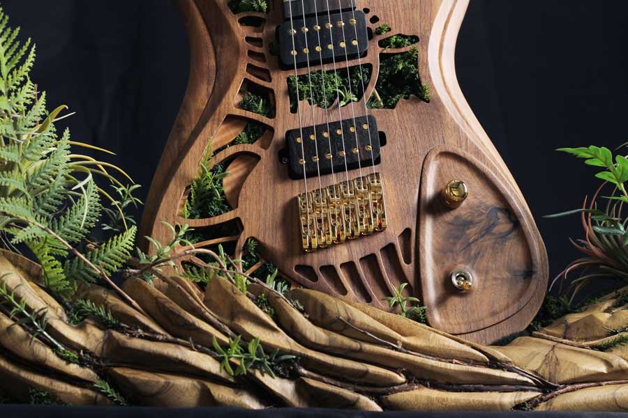 Imagine Prompt, a Boutique Guitar Showcase NAMM art installation. A wooden electric guitar surrounded by green foliage and draped with brown cloth.