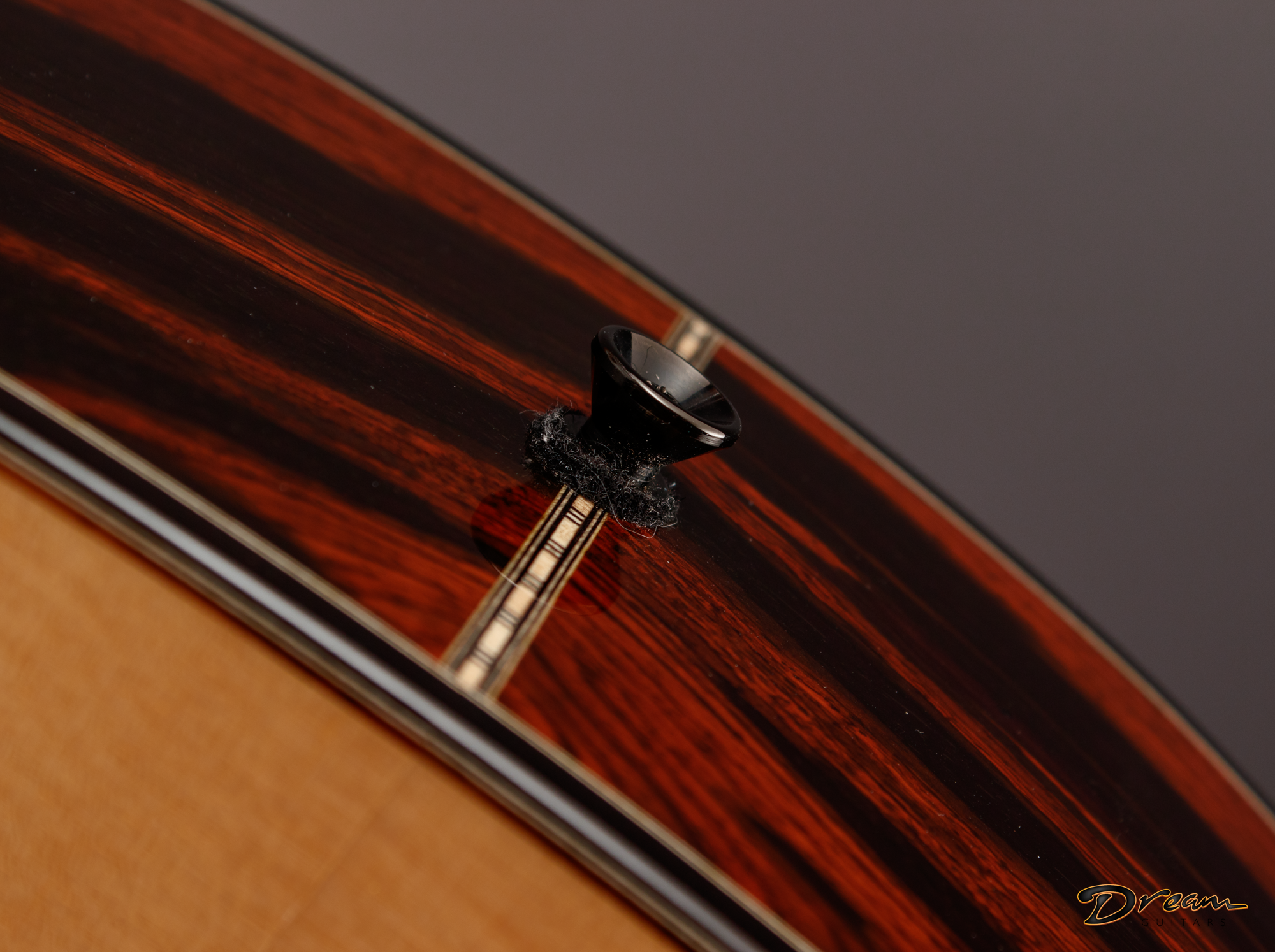Close-up of the side of a Laskin acoustic guitar, showing the wood grain and sound hole with a bridge pin. The guitar has a dark, polished finish with a reddish-brown hue.