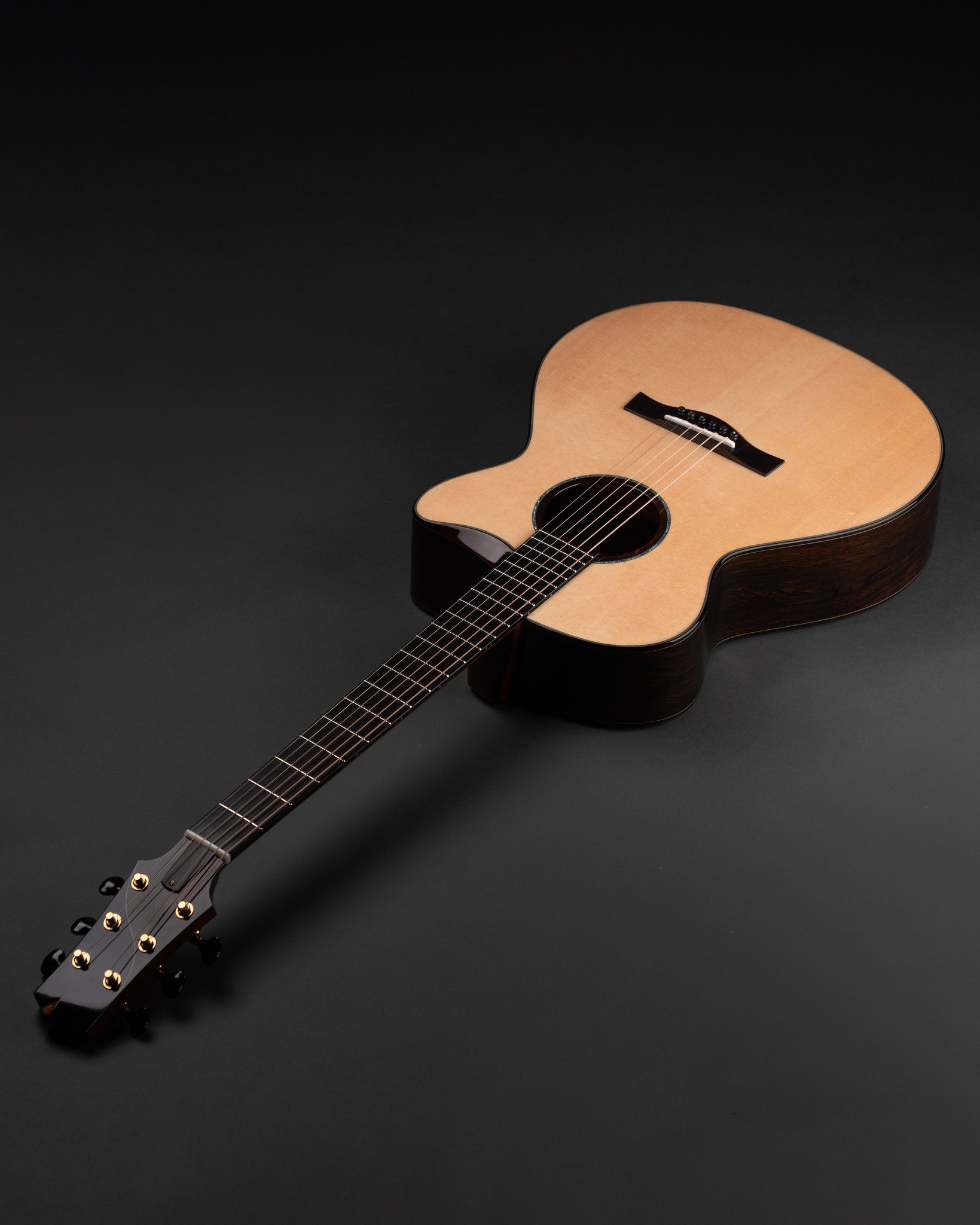 An Isaac Jang acoustic guitar with a light wood top and dark wood sides and neck lying on a black surface.