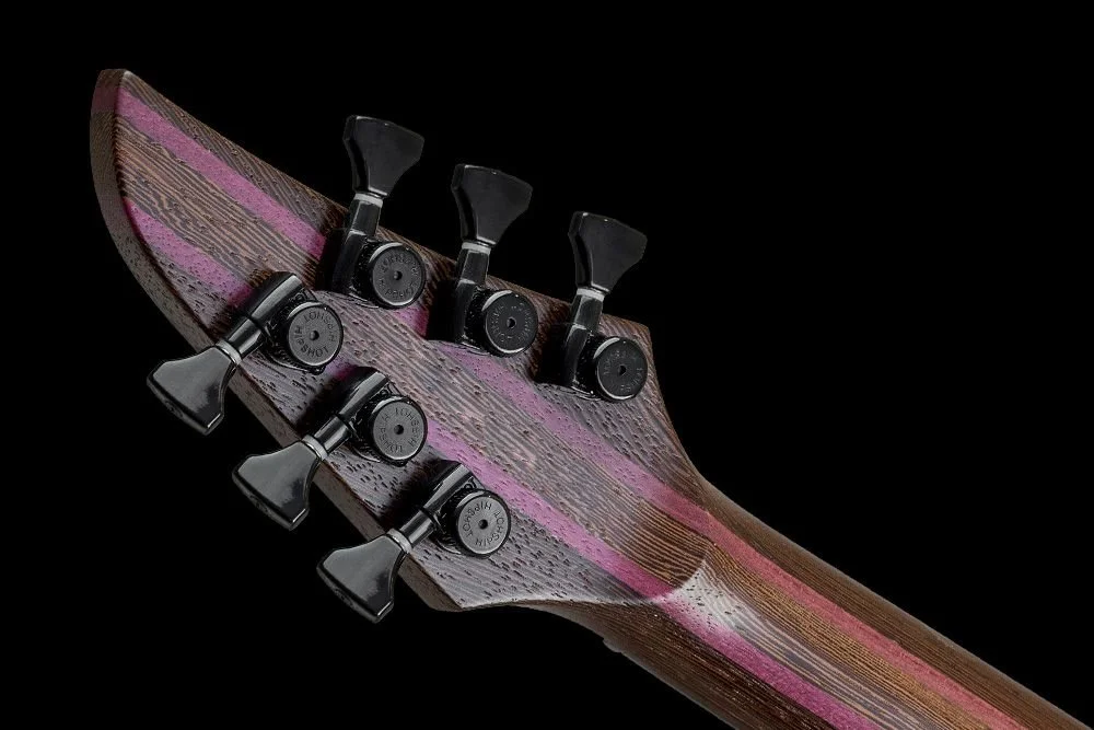 Close-up of the Mayones headstock of a guitar with eight tuning pegs, made of wood with a striped pattern, against a black background.