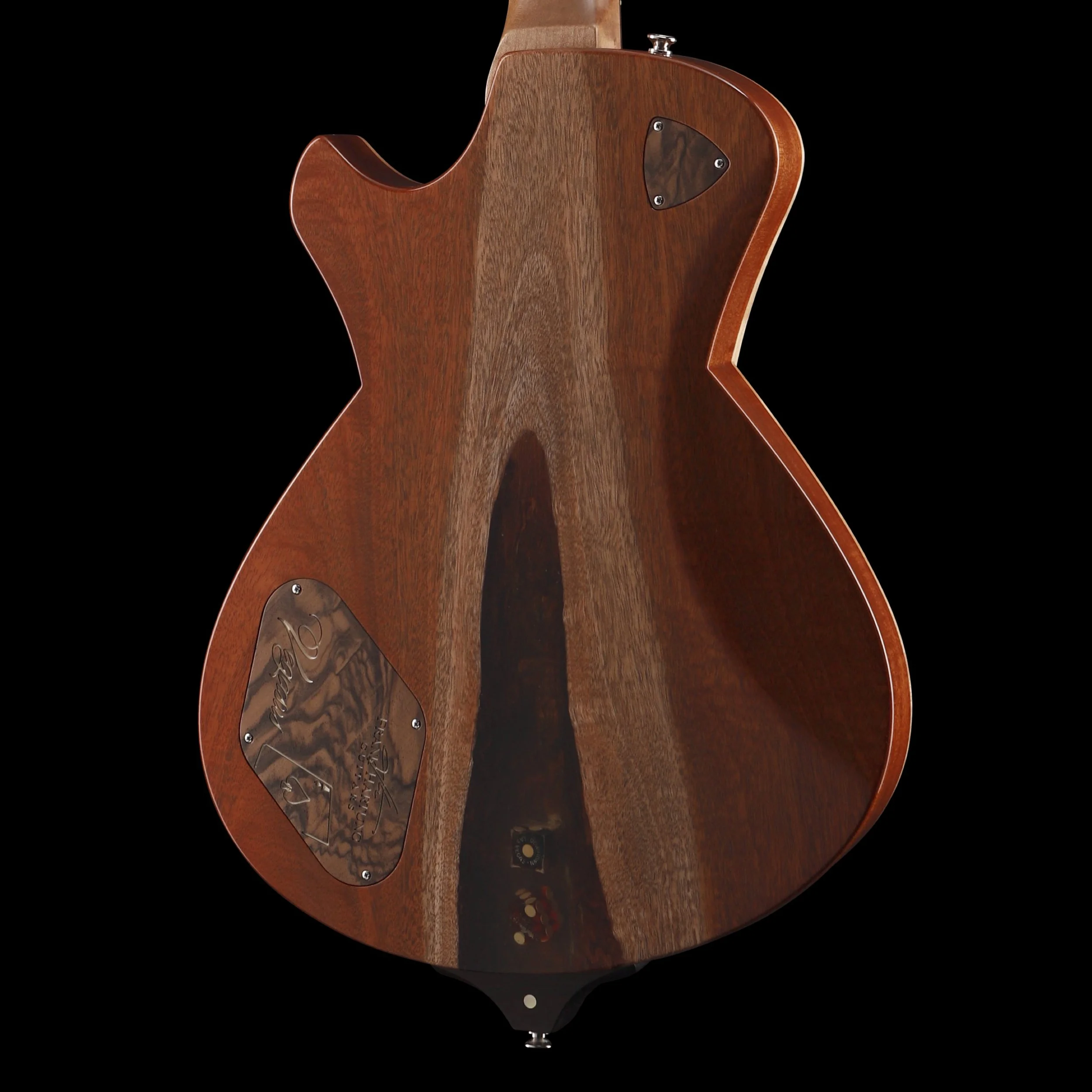 Back of a wooden Frank Hartung electric guitar with a glossy finish and two metal plates on the body, set against a black background.