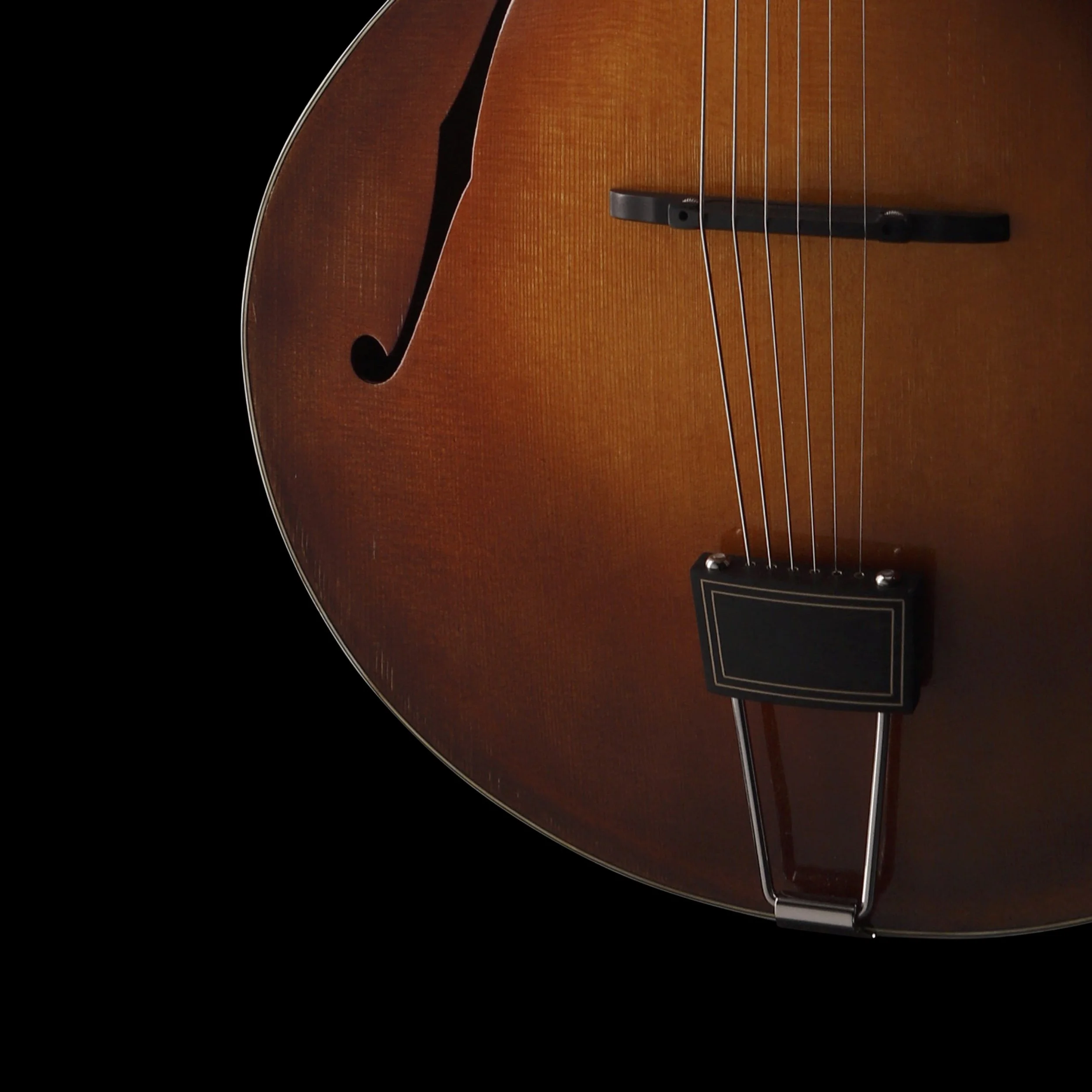 Close-up of a Cedar Mountain brown acoustic guitar body with six strings and a black pickguard against a black background.