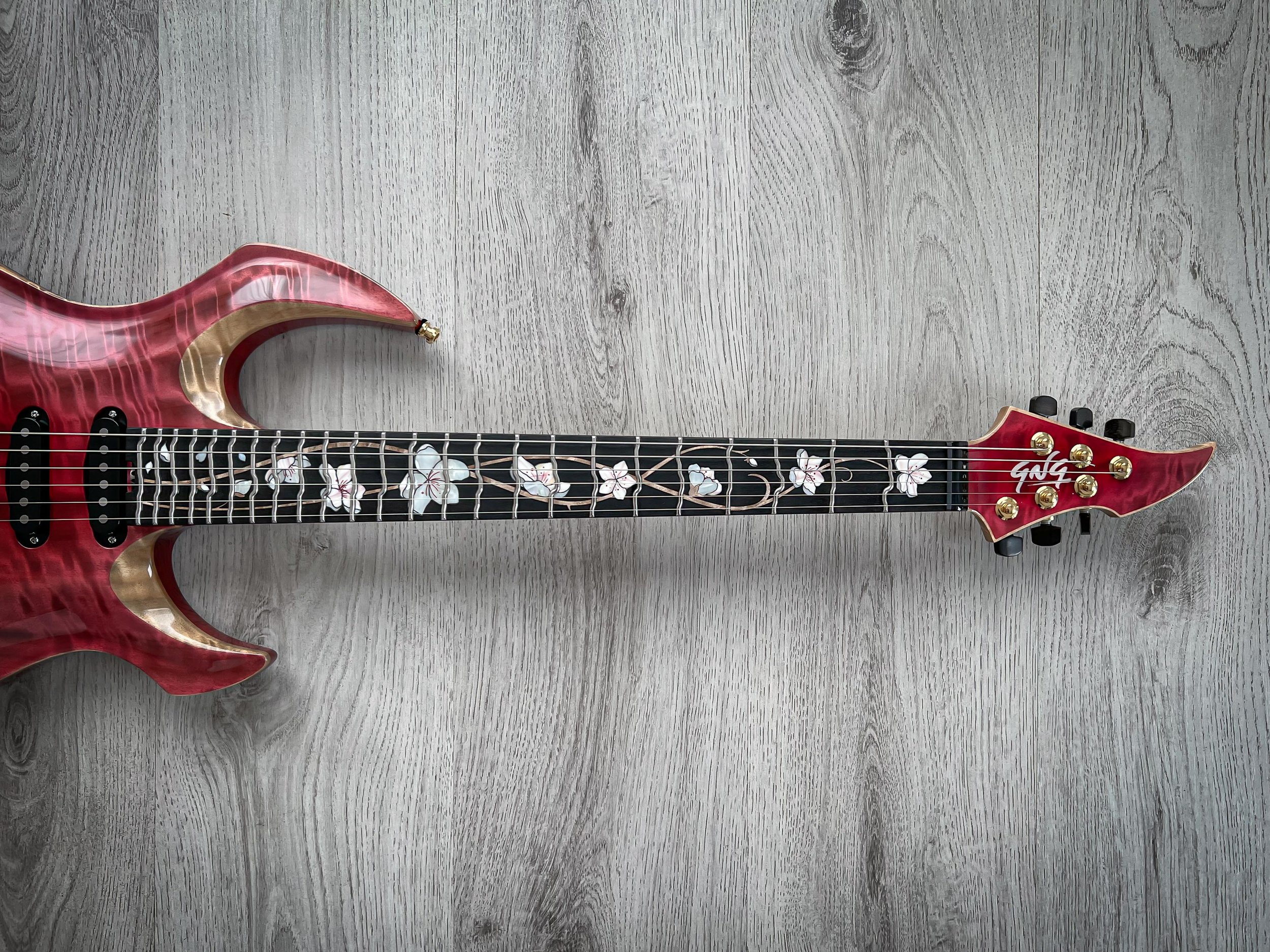 Red GNG Giulio Negrini electric guitar with floral inlay on fretboard and gold tuning pegs on a light wood floor