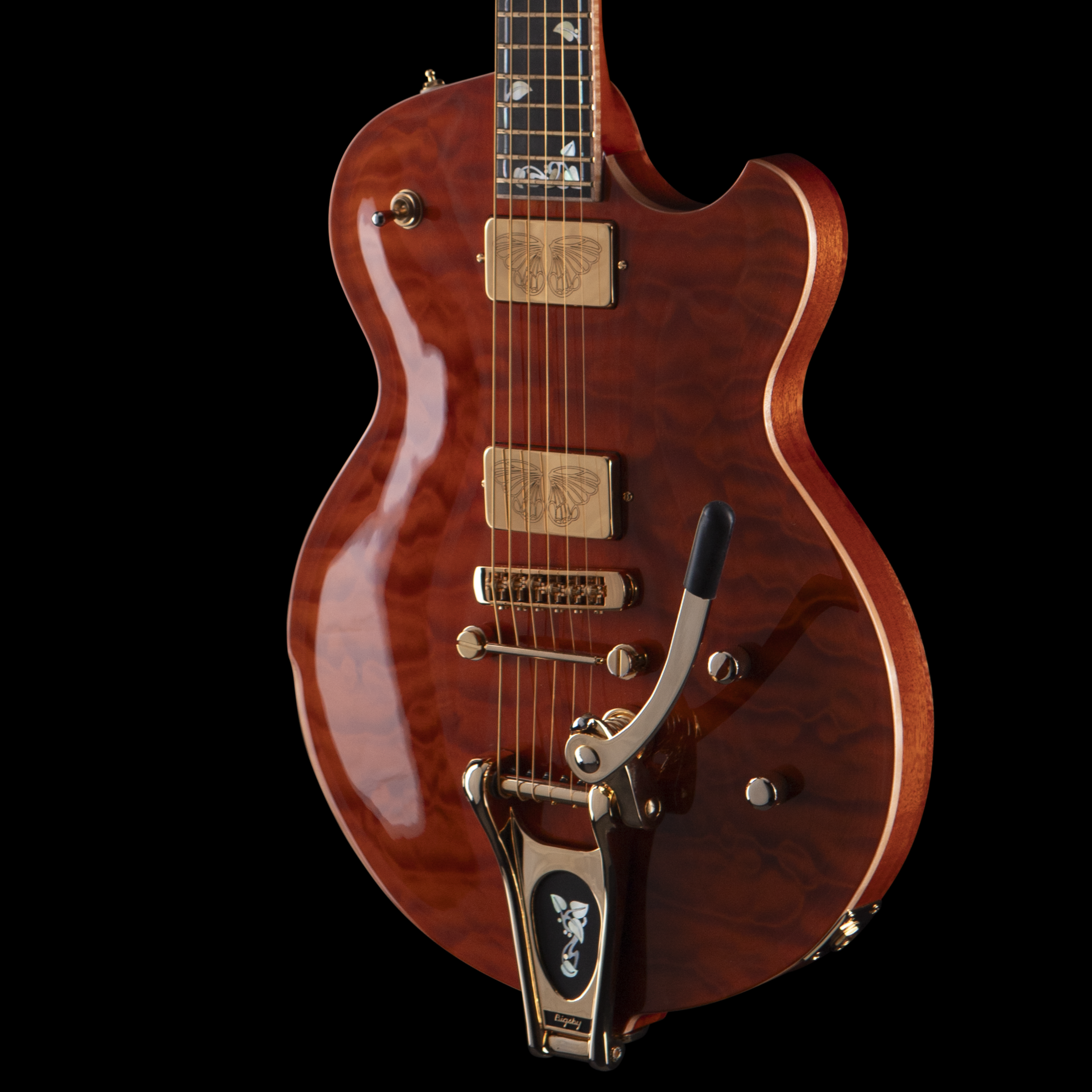 Close-up view of a mahogany-colored electric Djerjinski guitar with gold hardware and butterfly inlays on the fretboard, set against a black background.