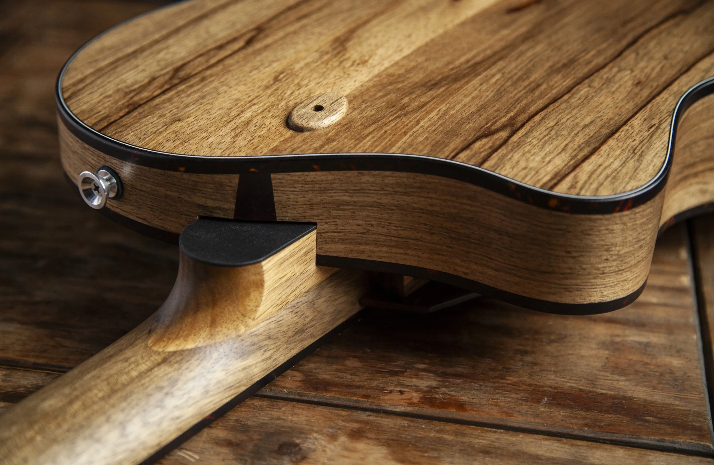 Close-up view of a wooden Island Instruments guitar on a wooden surface, showing the instrument's body and neck with tuning pegs.