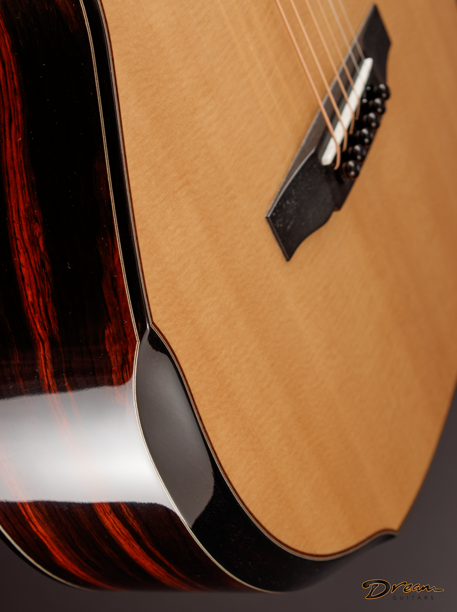 Close-up of the body and strings of an acoustic Laskin guitar with a wood grain finish, against a black background, with a "Dream Guitars" logo in the bottom right corner.