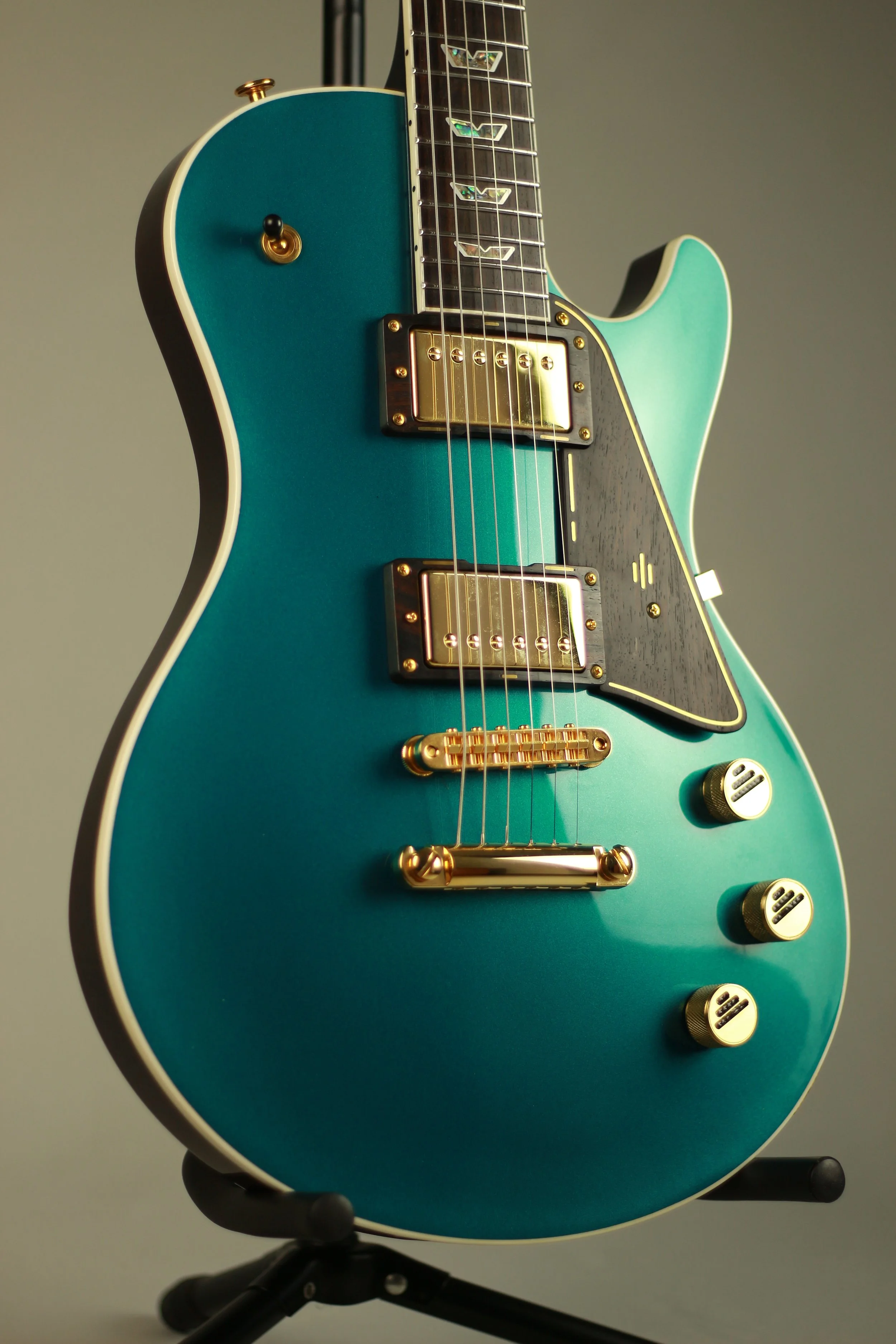 Close-up of an electric Corsell guitar with a teal body, black pickguard, gold hardware, and three control knobs, mounted on a black stand.