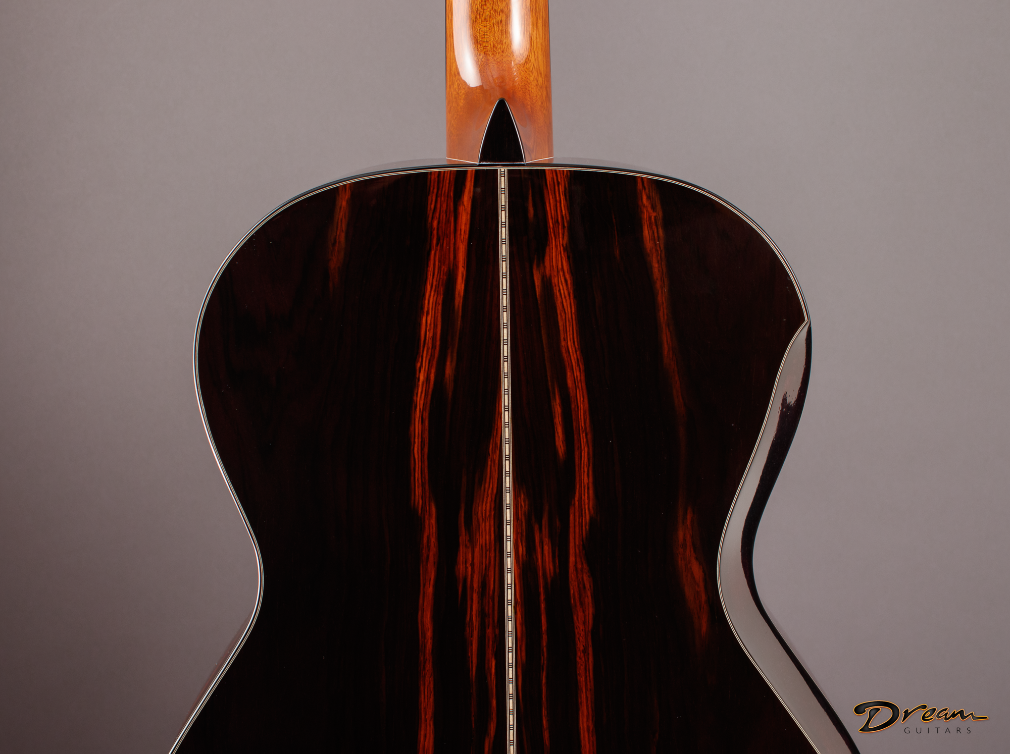 Close-up of the back of a wooden Laskin acoustic guitar with a focus on the wood grain and string divider, against a plain gray background. The guitar has a glossy finish and a signature logo in the bottom right corner.