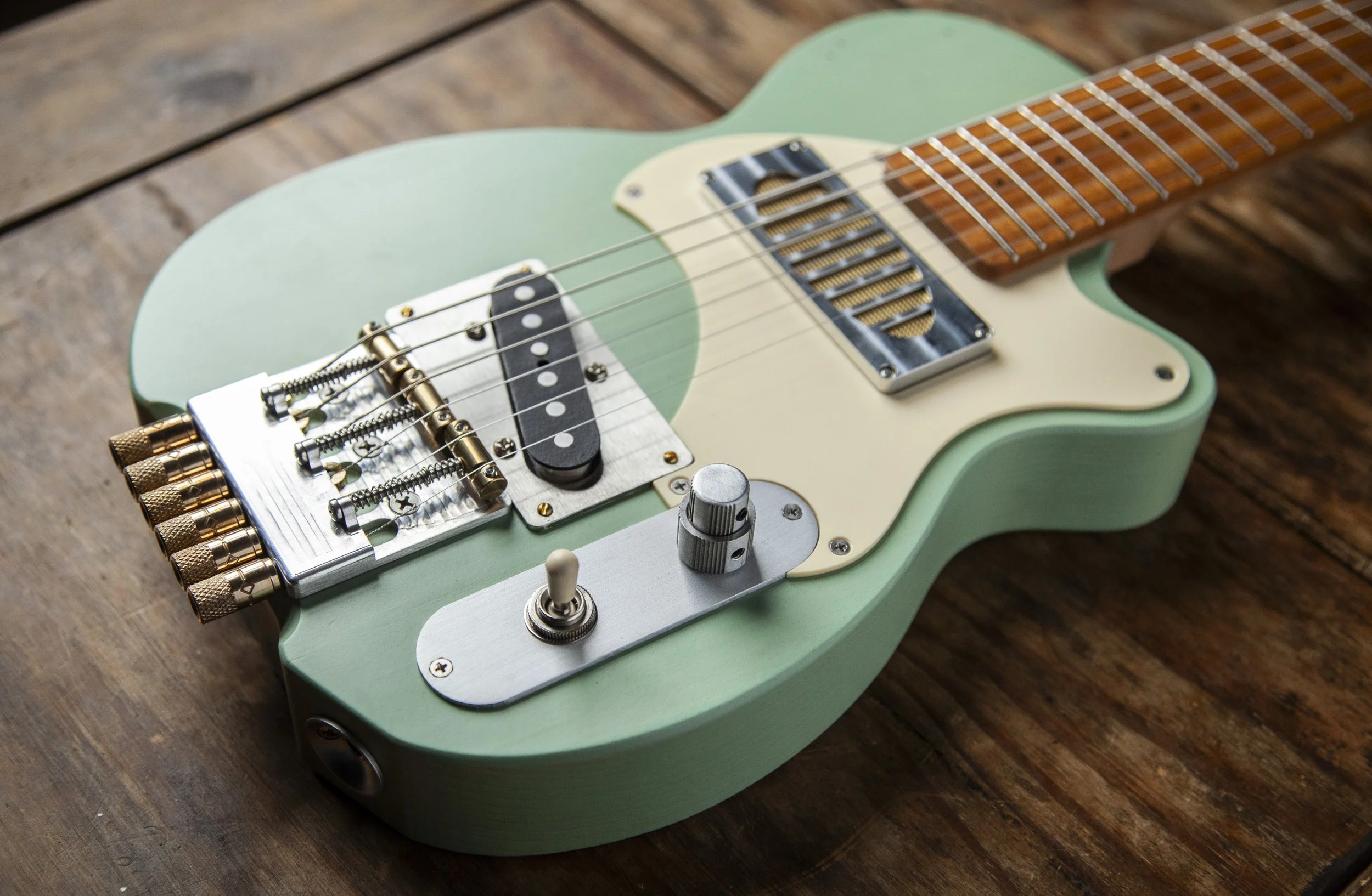 A light green electric Island Instruments guitar resting on a wooden surface, showing close-up of the hardware, strings, and pickups.