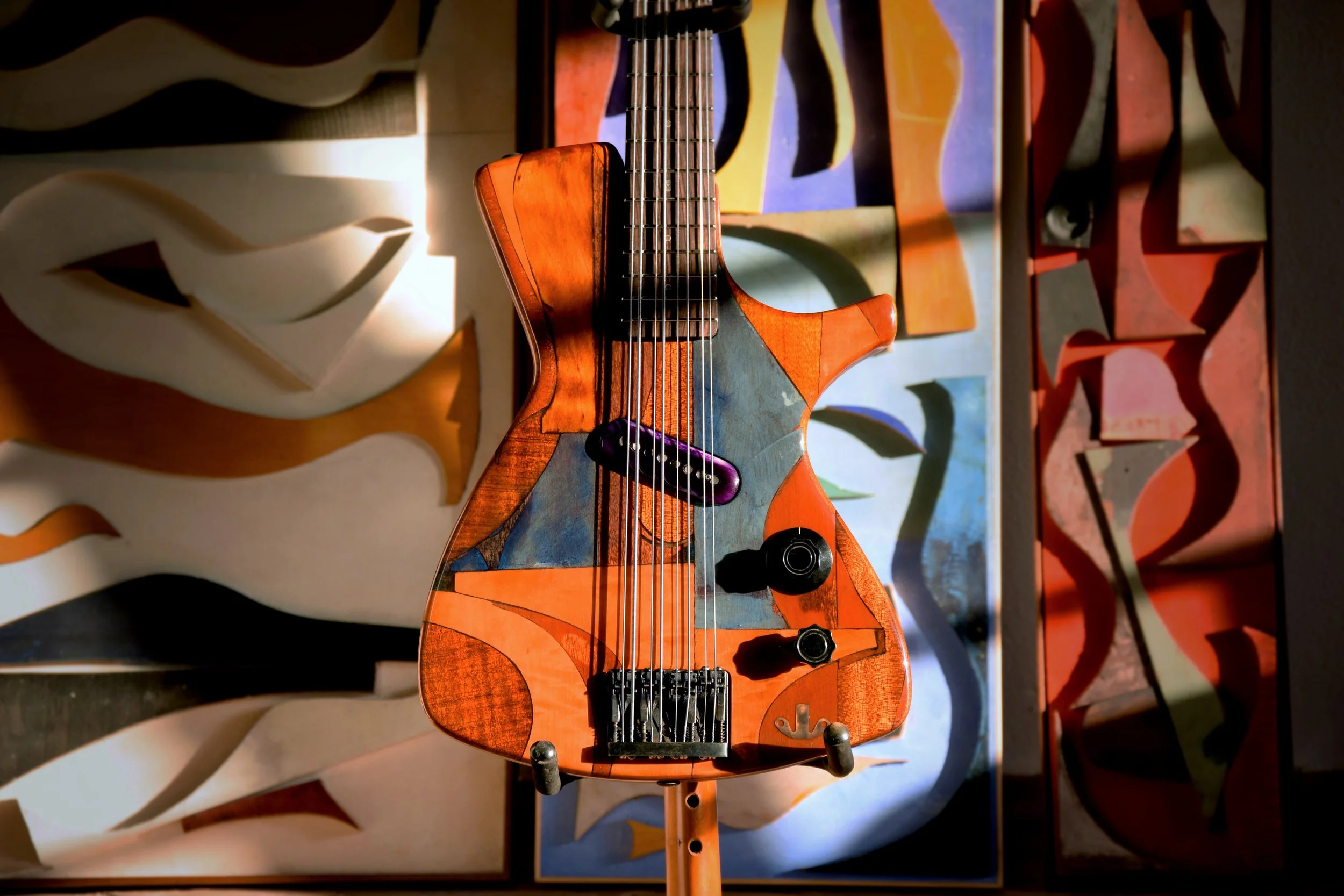 An electric Spalt guitar with a colorful, abstract design on its body, standing against a wall with various art pieces.