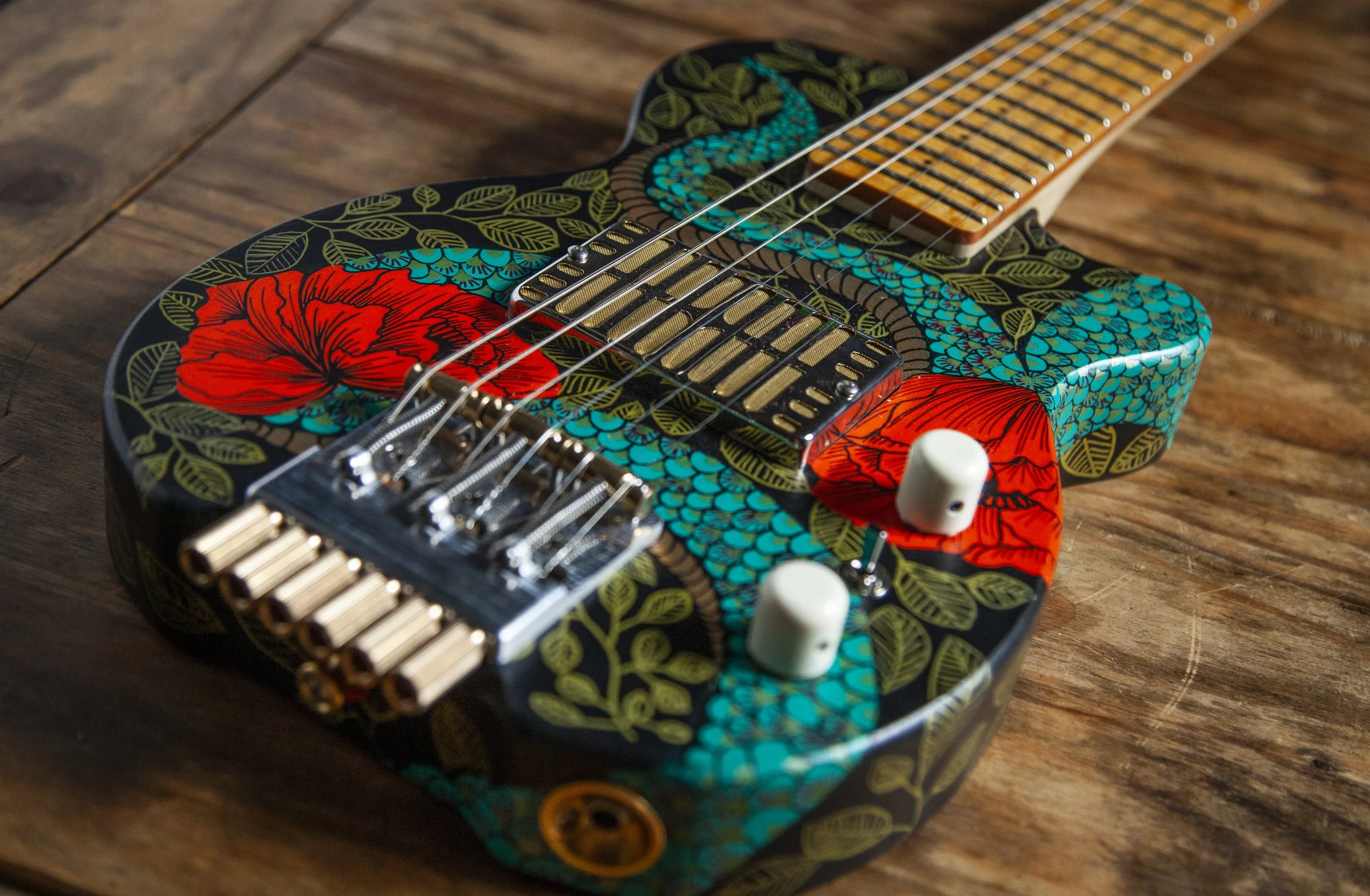A close-up of an electric Island Instruments guitar with a colorful floral and leaf pattern painted on its body, resting on a wooden surface.