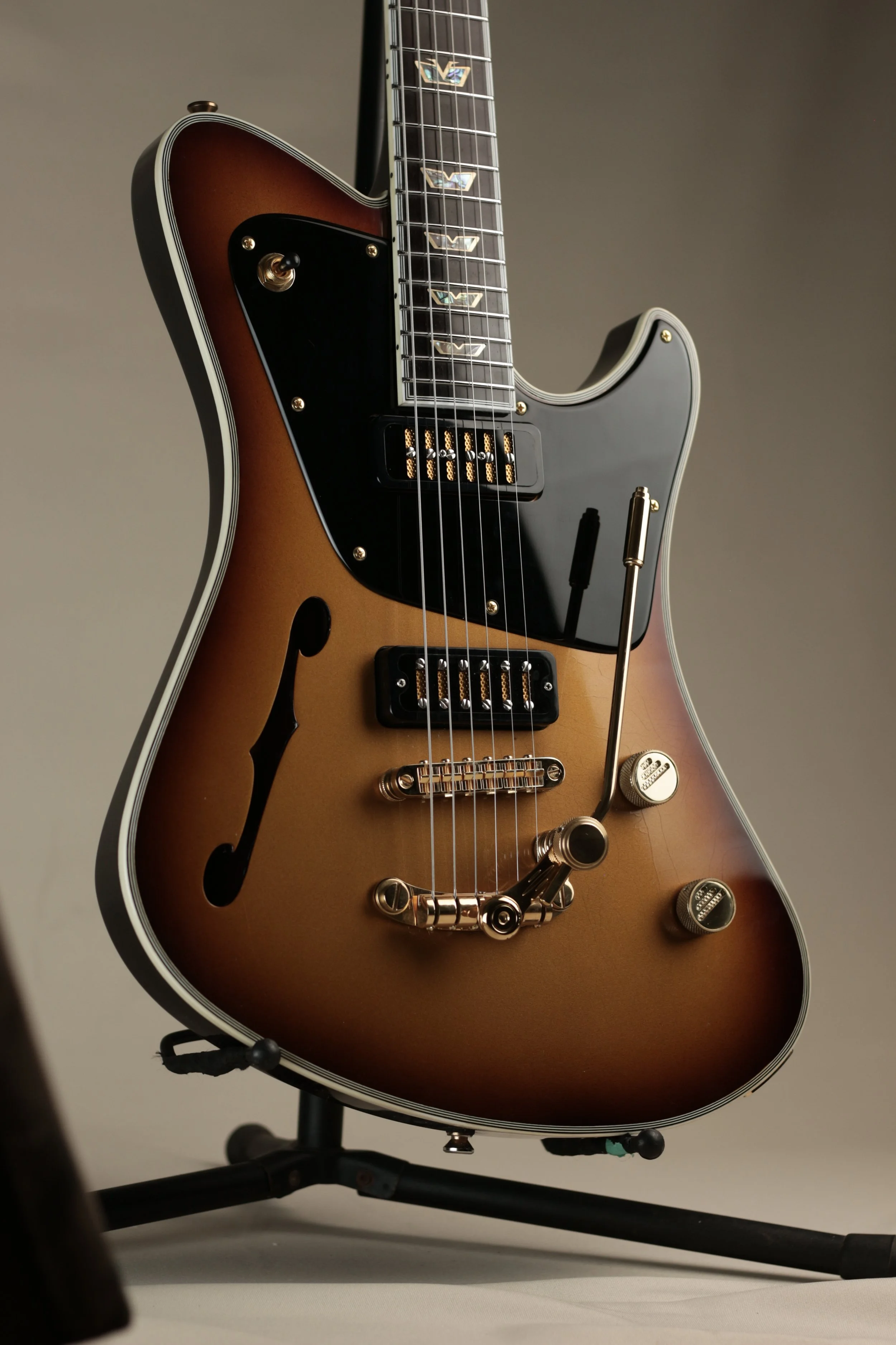 A semi-hollow electric Corsell guitar with a sunburst finish, black pickguard, and gold hardware, resting on a black stand.