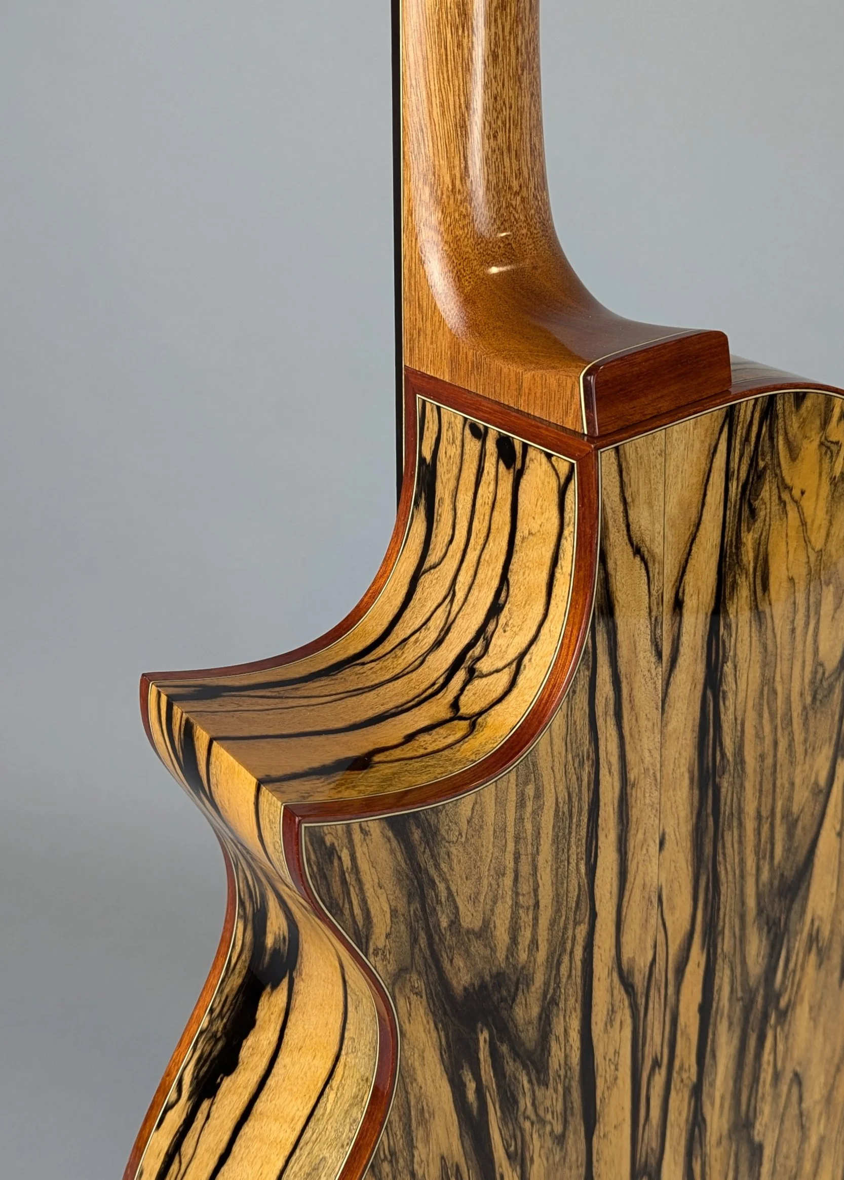 Close-up of the side and neck of a Morgan Kelsey electric guitar with intricate wood grain patterns and a smooth, polished finish.
